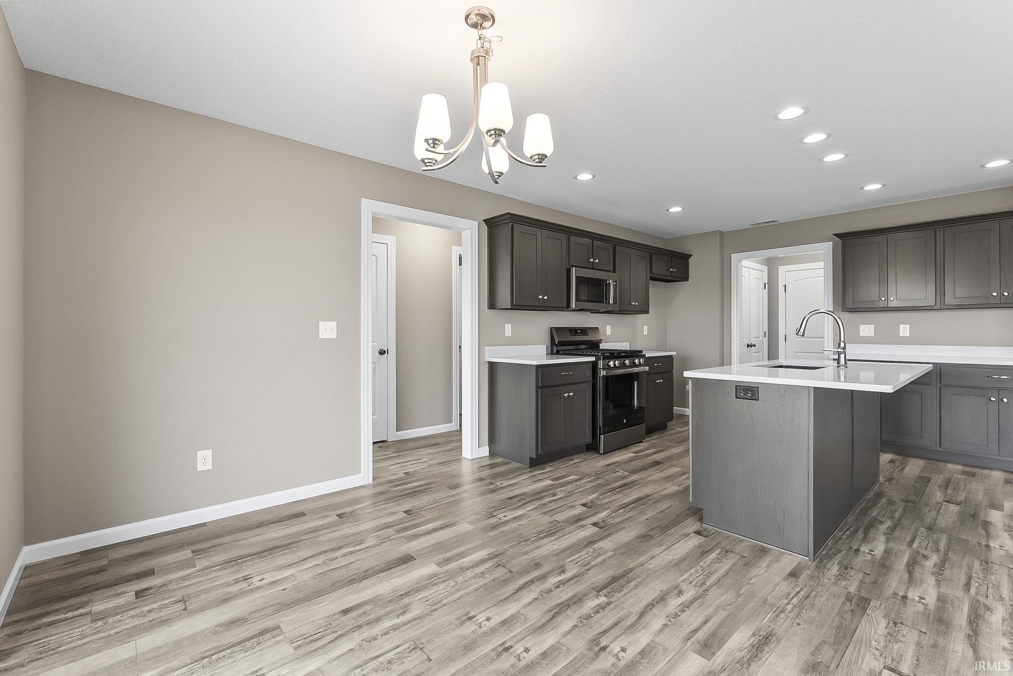 Kitchen with stainless steel appliances, an island with sink, light wood-style flooring, light stone countertops, and a chandelier