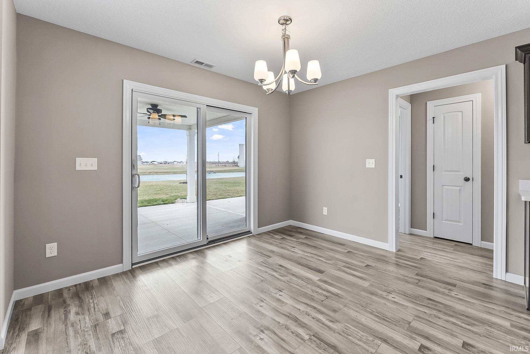 Unfurnished dining area with a water view, a chandelier, light wood-type flooring, and ceiling fan
