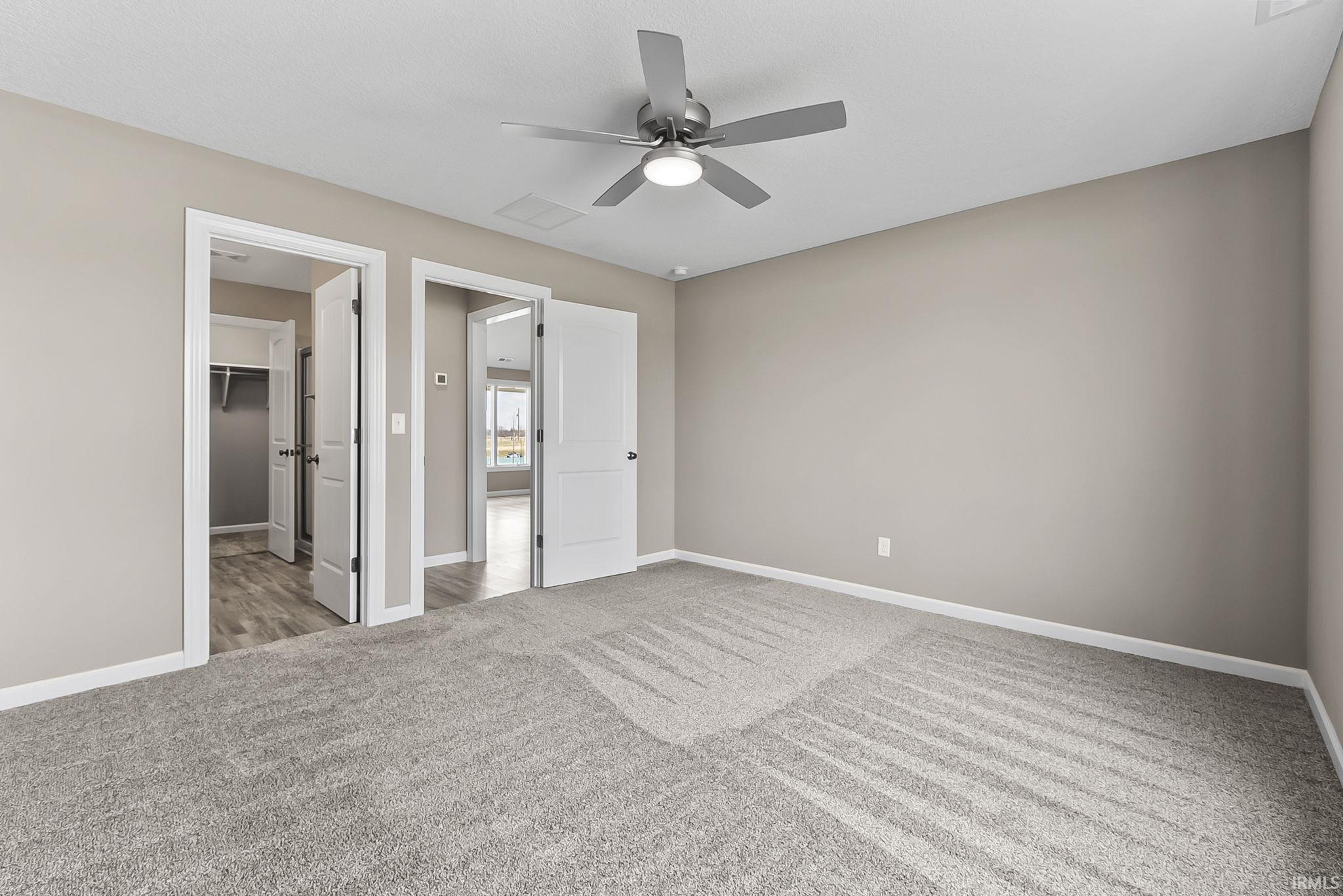 Unfurnished bedroom with a spacious closet, light colored carpet, and a ceiling fan