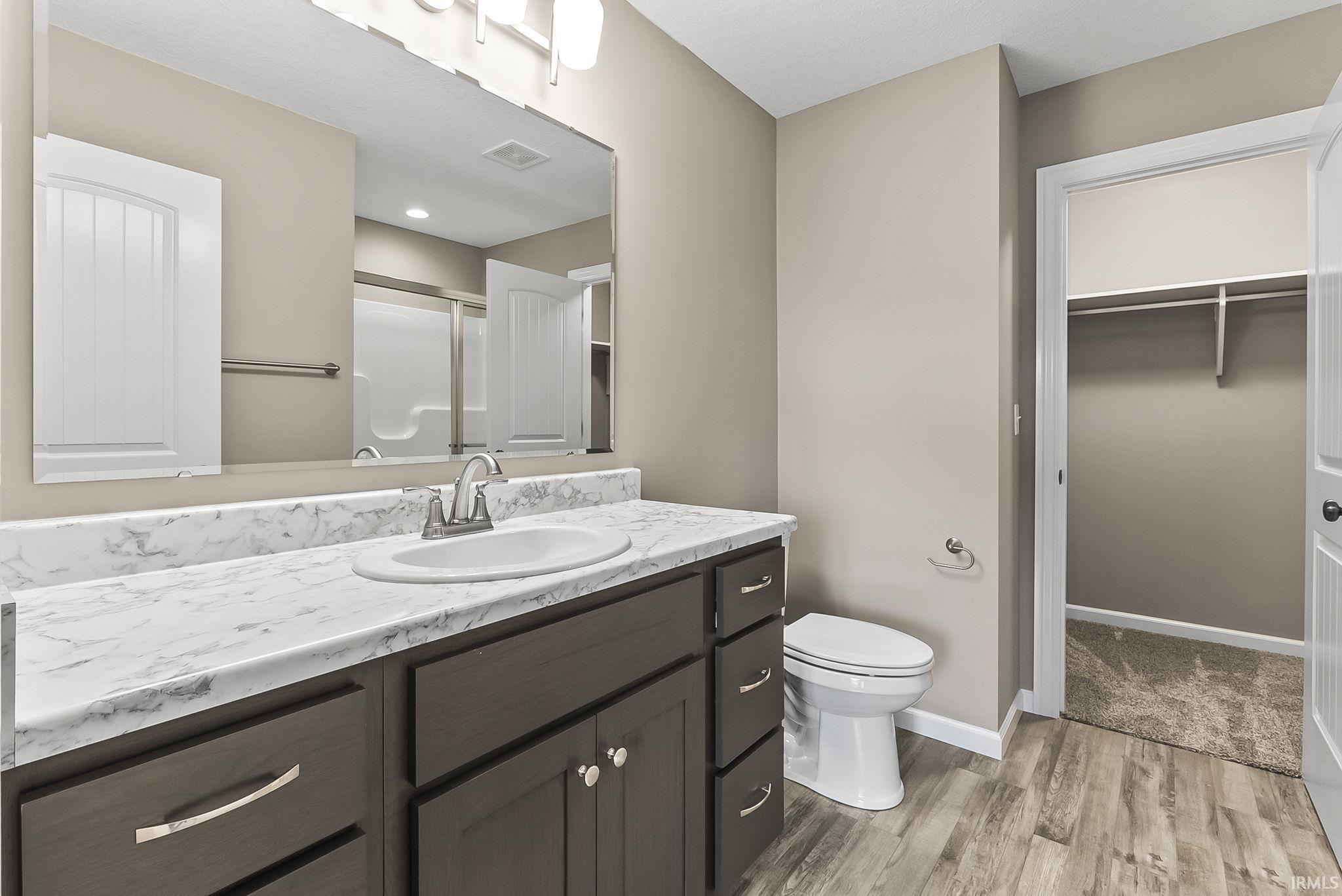Full bathroom featuring a stall shower, a walk in closet, vanity, and light wood-style floors