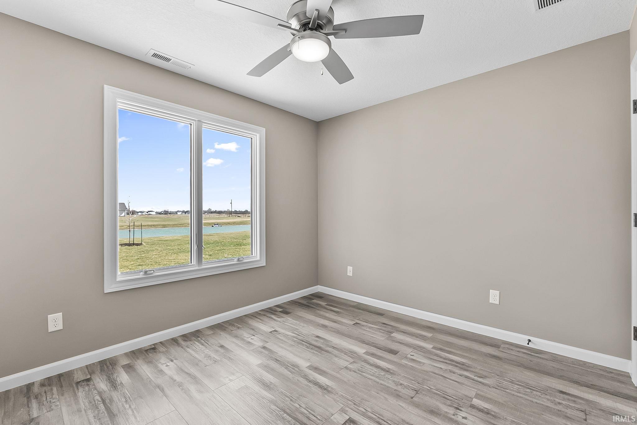 Spare room with a water view, a ceiling fan, and light wood-style flooring