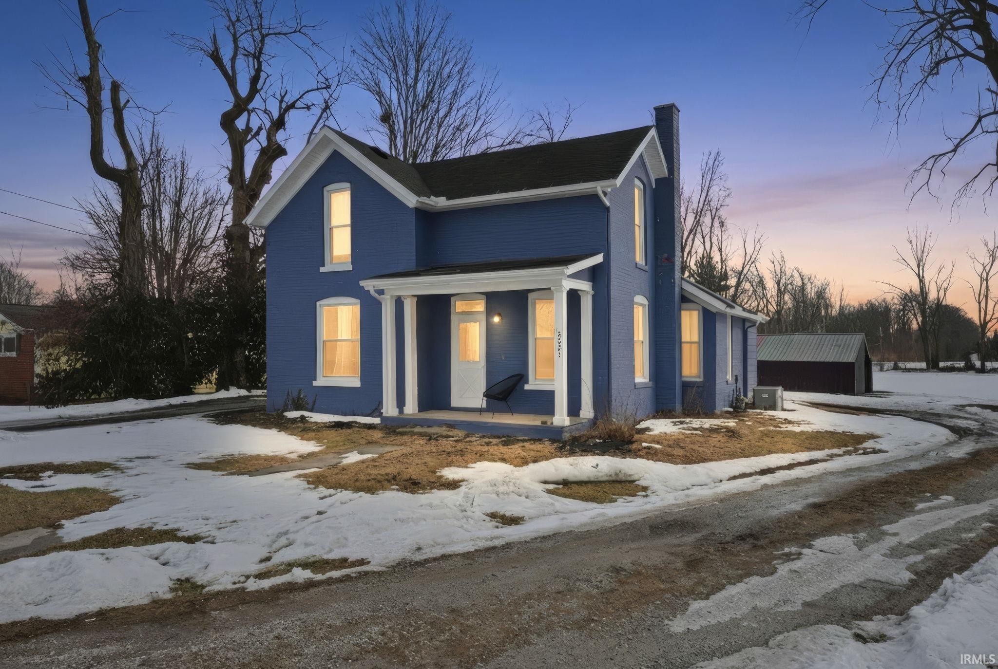 View of front of home featuring a porch, a chimney, and an outdoor structure