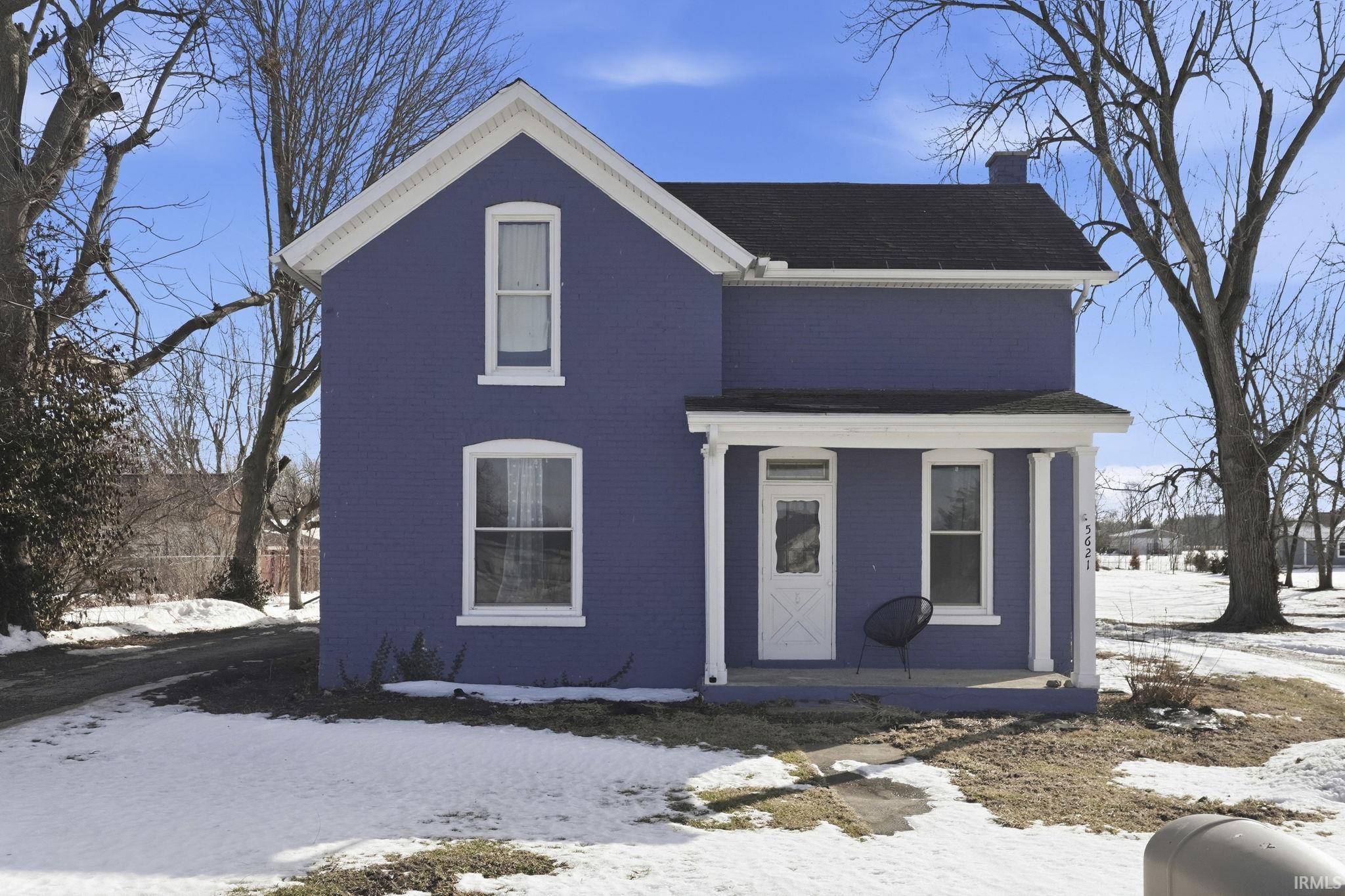 View of front facade with a chimney, brick siding, and covered porch
