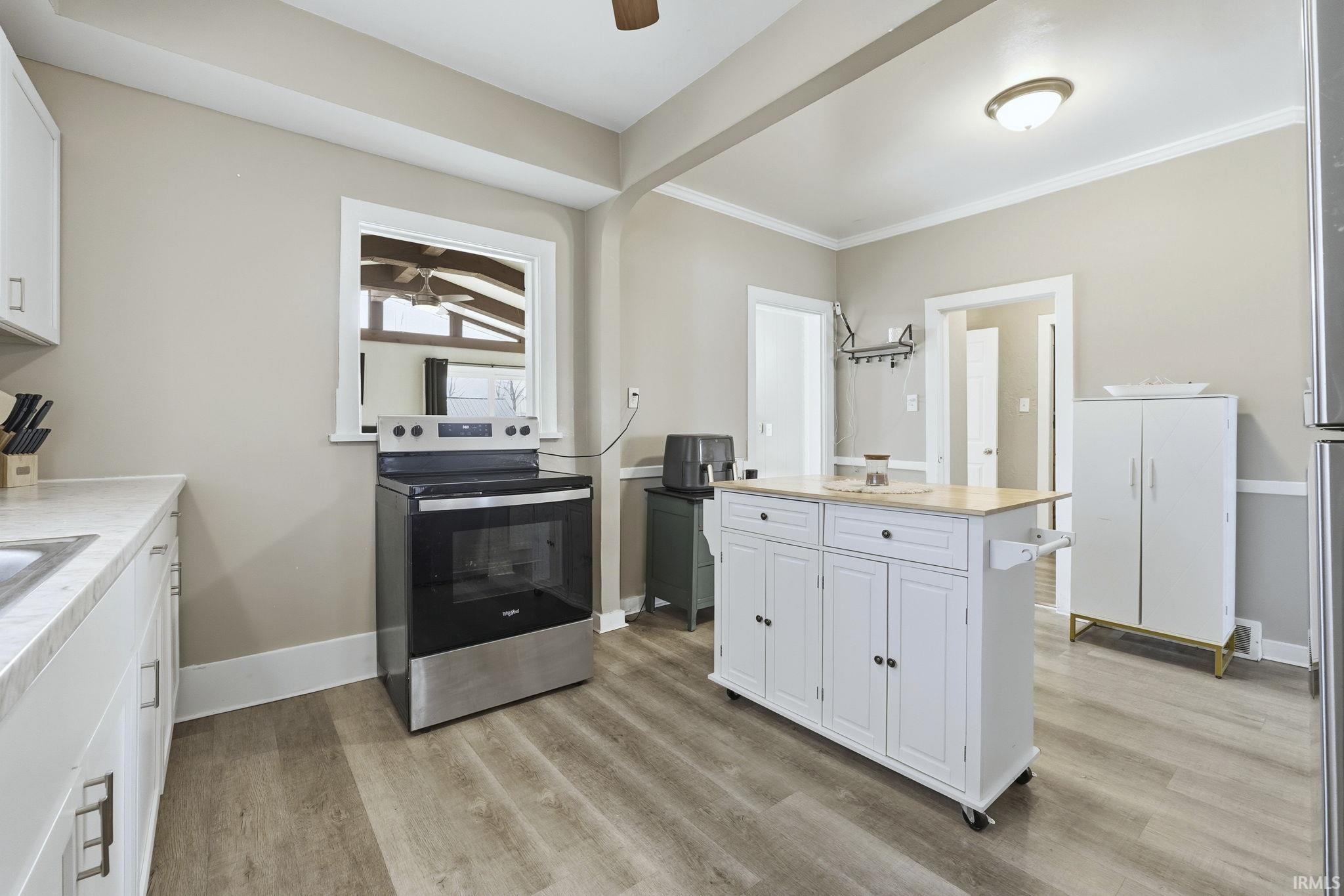 Kitchen featuring white cabinets, stainless steel electric stove, light countertops, light wood-style floors, and crown molding