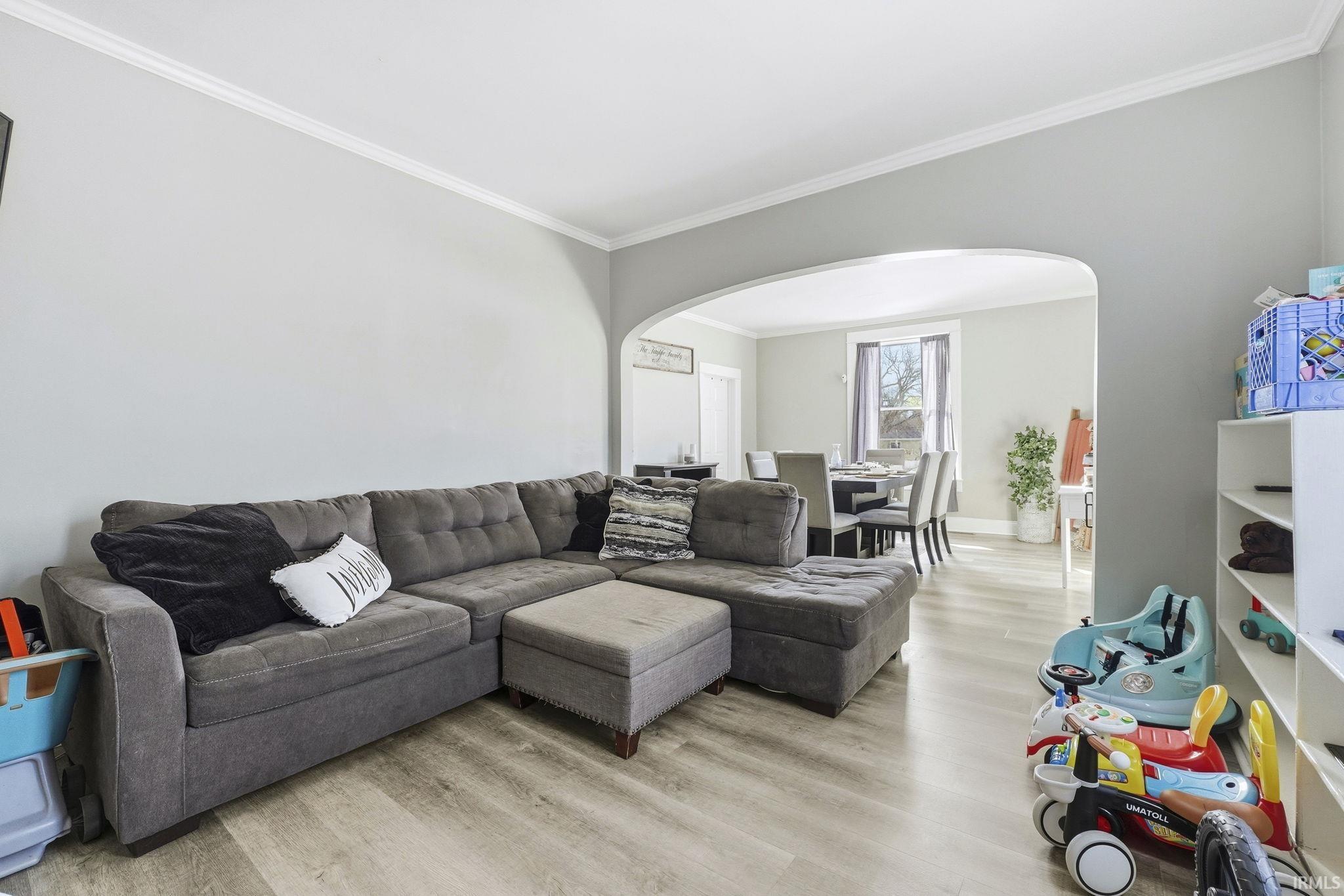 Living room with light wood-style floors, crown molding, and arched walkways