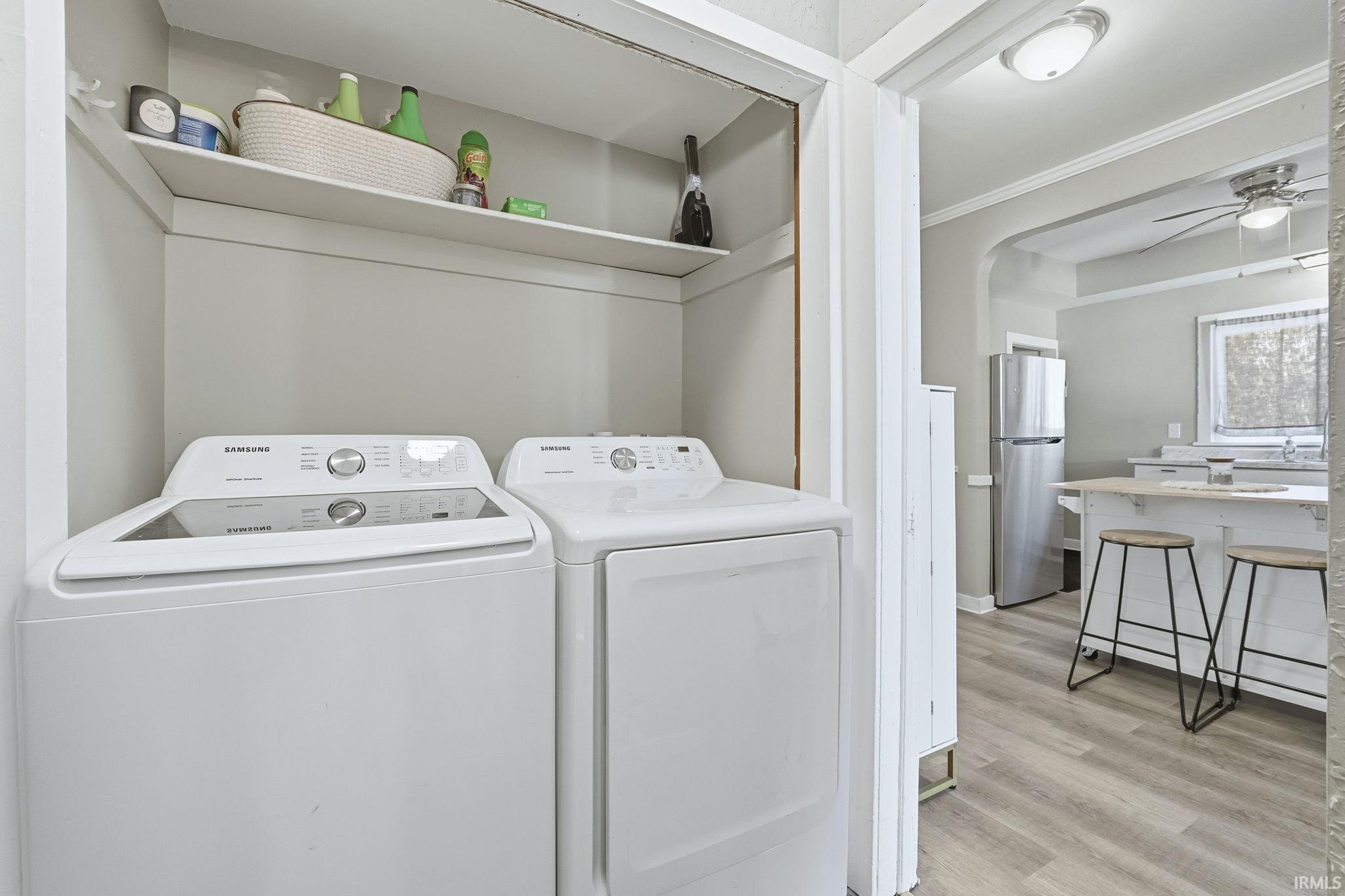 Laundry area with arched walkways, separate washer and dryer, light wood-style flooring, and a ceiling fan
