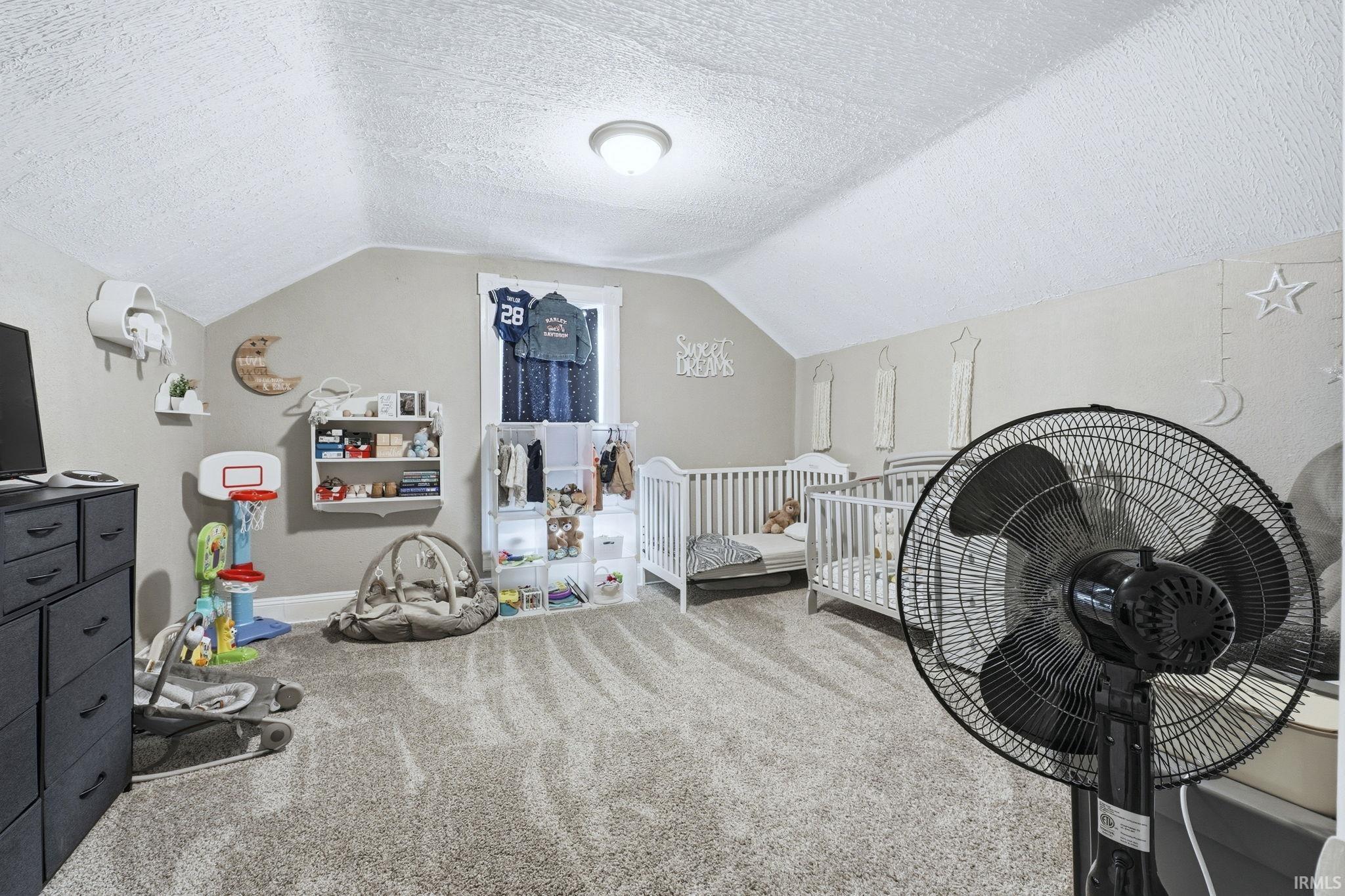 Carpeted bedroom featuring a textured ceiling and a nursery area