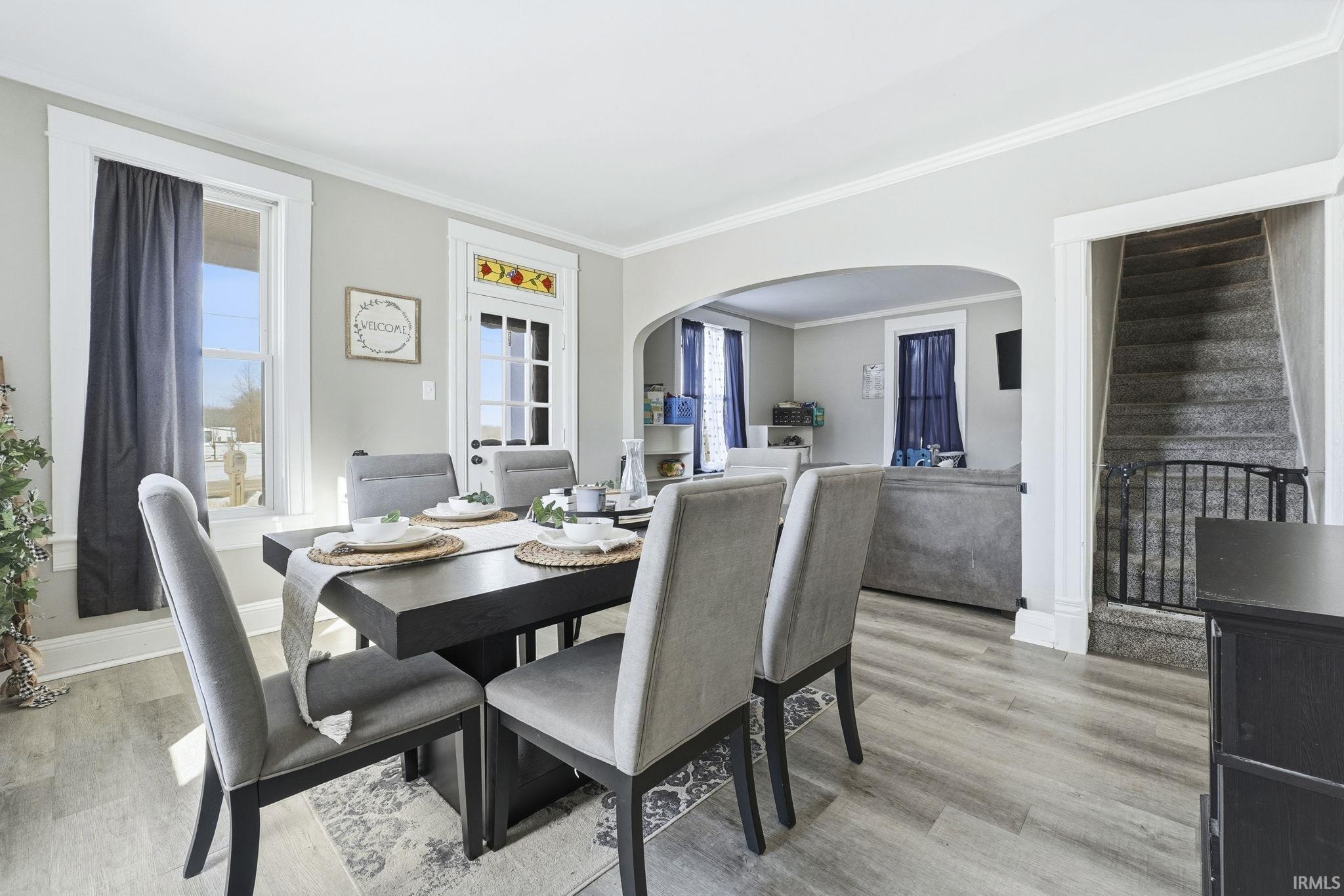 Dining room with arched walkways, light wood-type flooring, ornamental molding, and plenty of natural light
