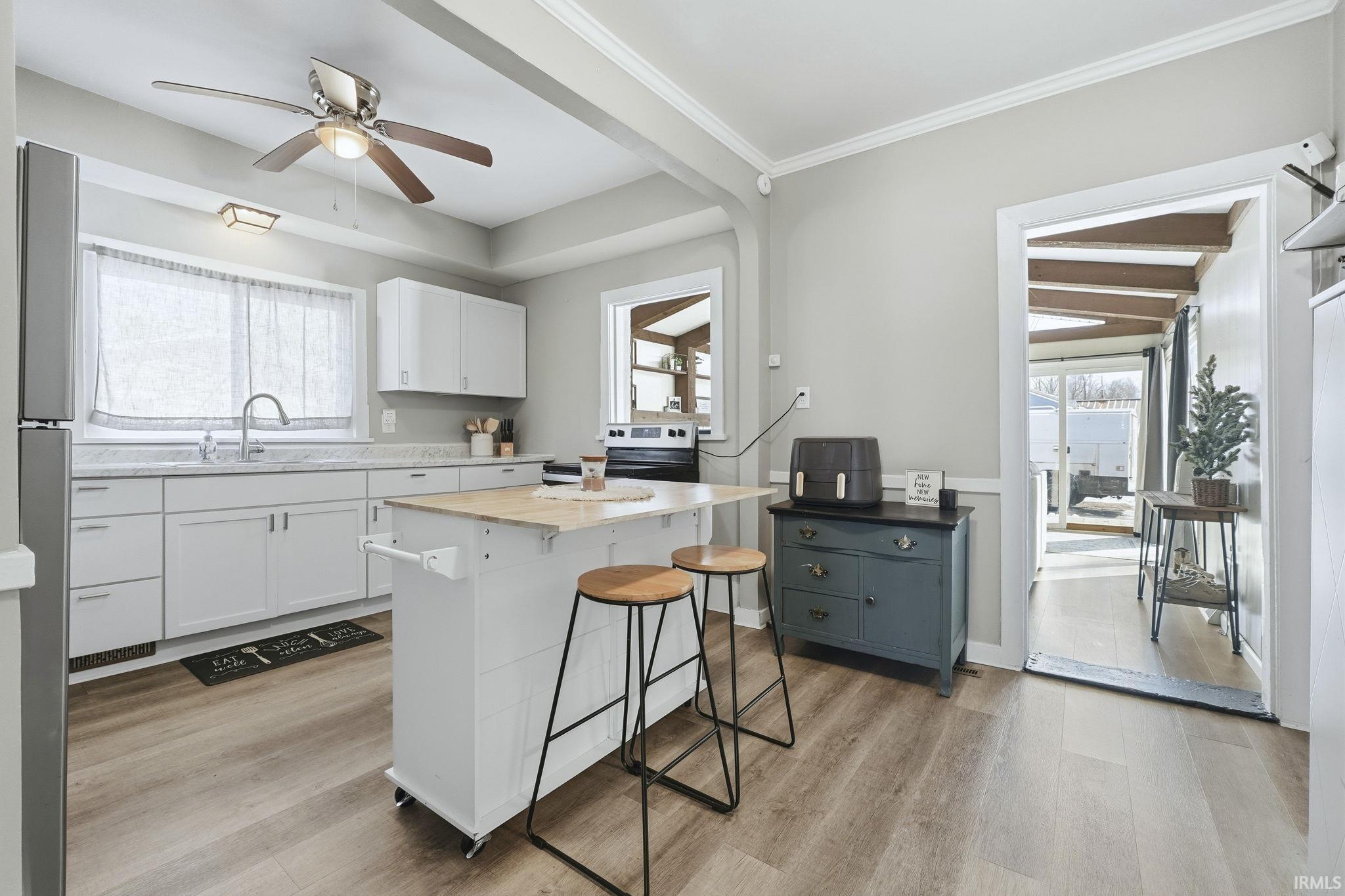 Kitchen with white cabinetry, healthy amount of natural light, a ceiling fan, a breakfast bar area, and ornamental molding