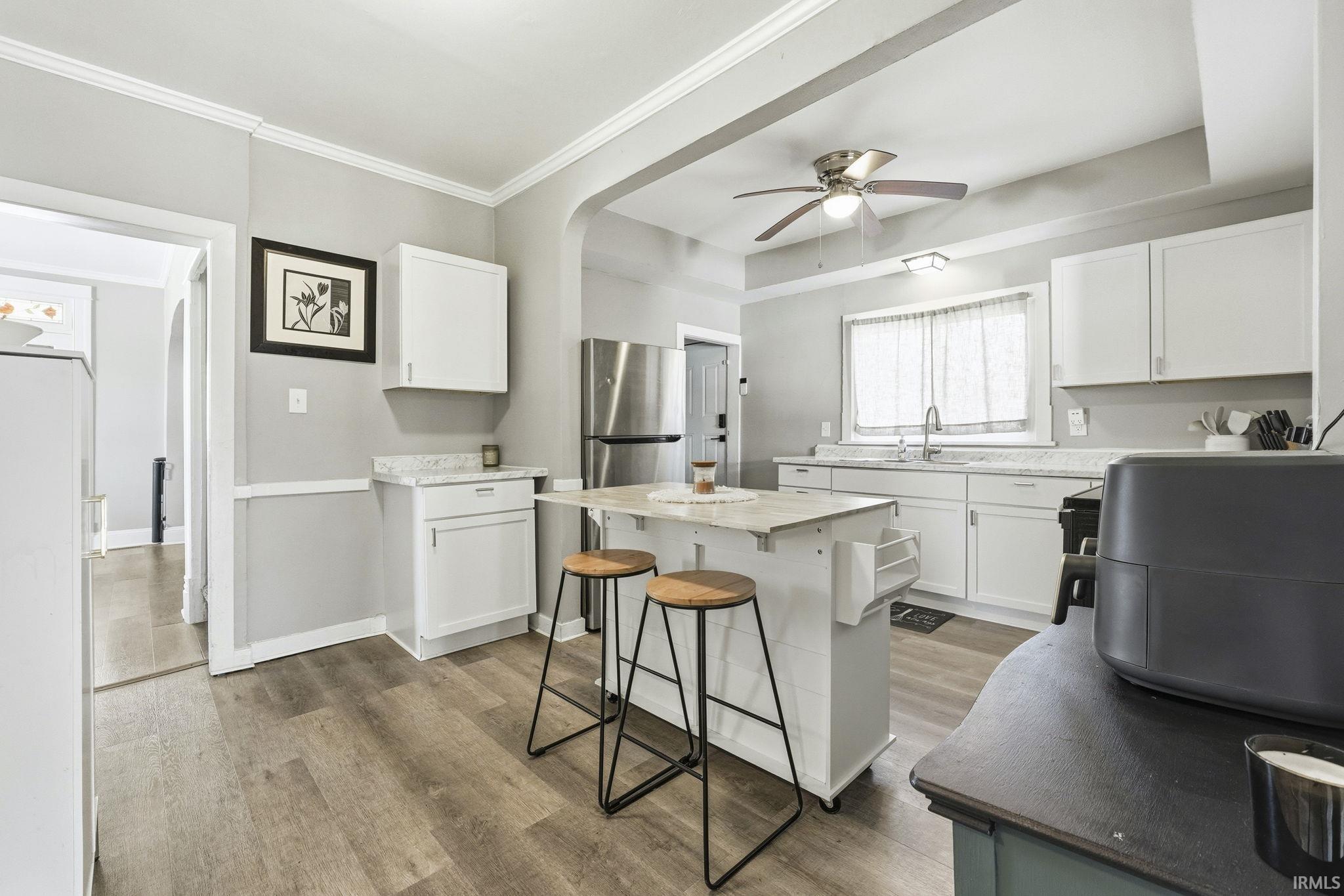 Kitchen with white cabinets, light wood-type flooring, freestanding refrigerator, ceiling fan, and crown molding
