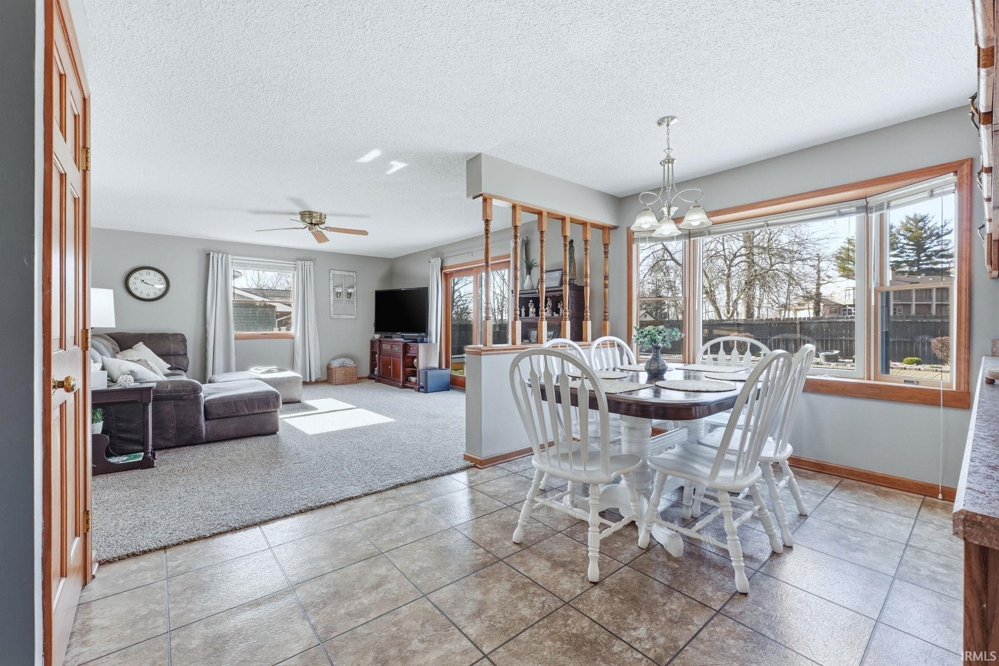Dining space featuring a chandelier, a textured ceiling, ceiling fan, light tile patterned floors, and light carpet