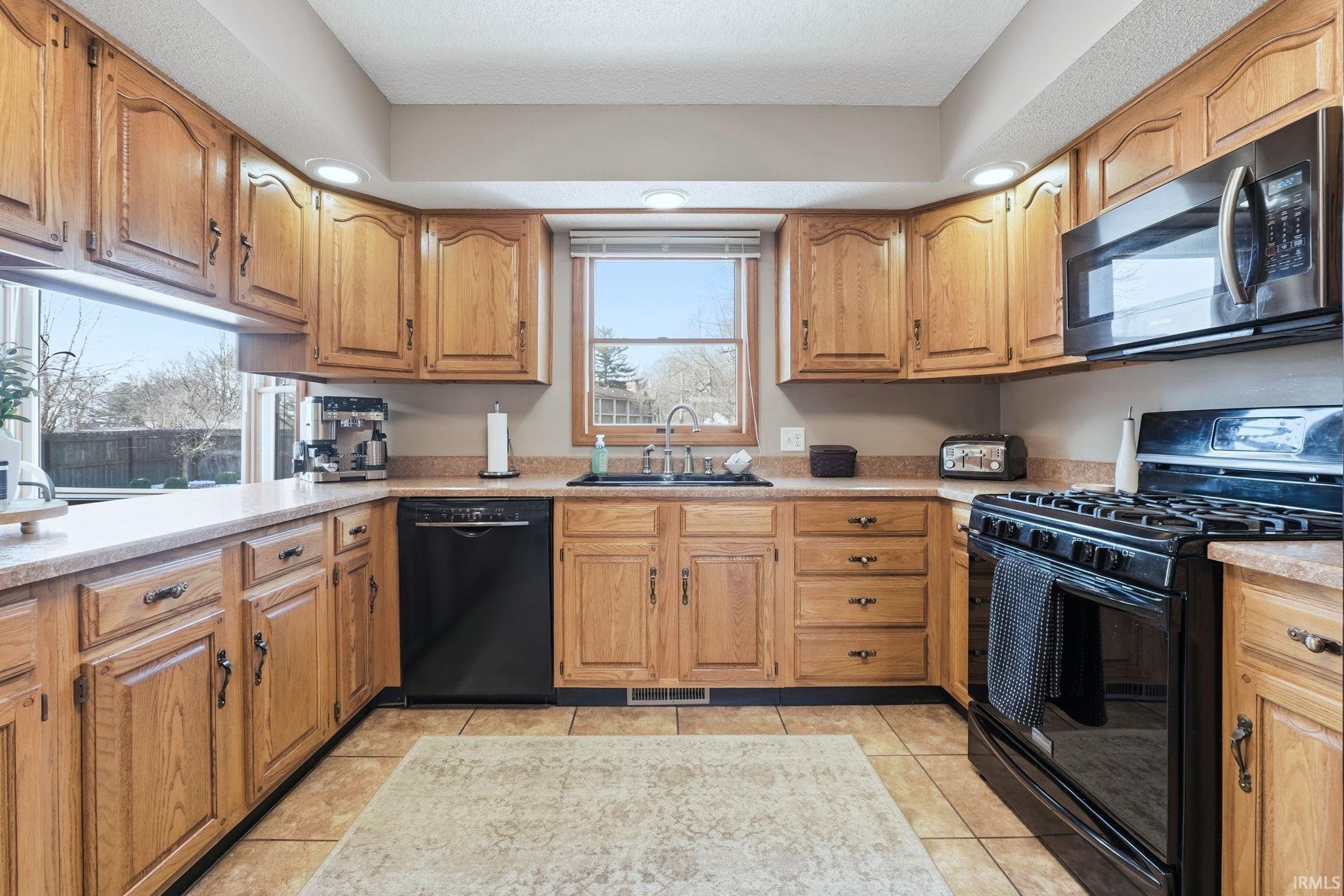 Kitchen with black appliances, wood finish cabinetry, recessed lighting, and light tile patterned floors