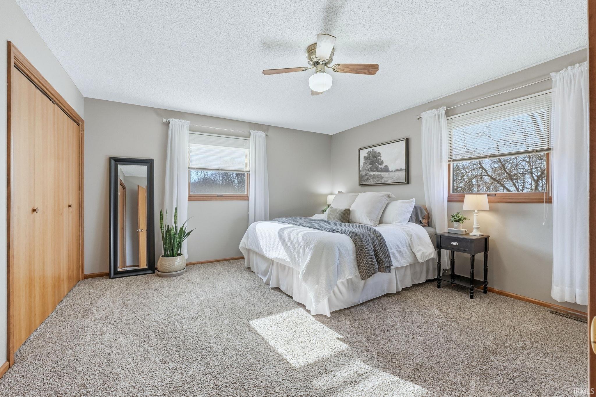 Bedroom featuring a closet, light colored carpet, a ceiling fan, and a textured ceiling