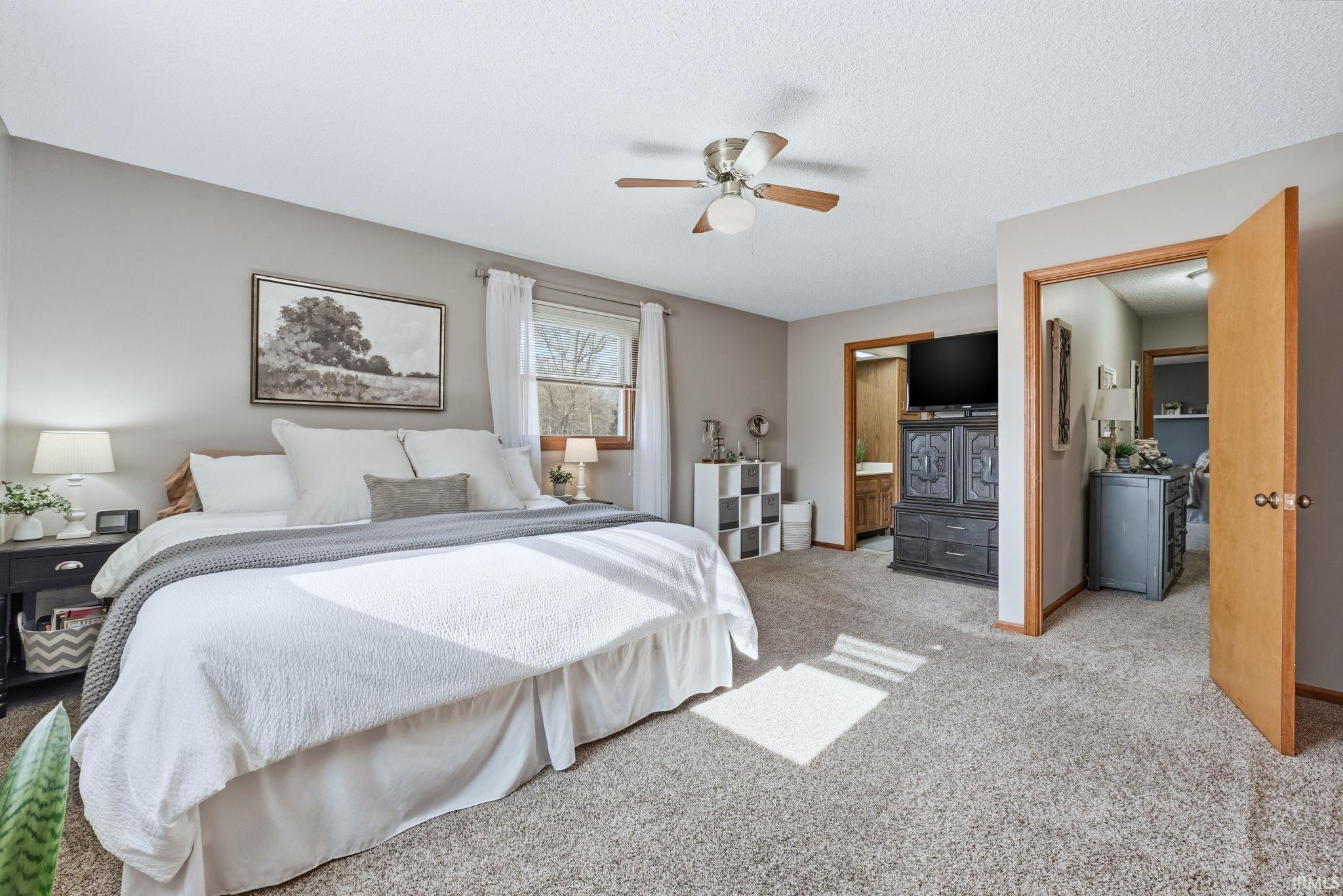 Bedroom with light colored carpet, a ceiling fan, and ensuite bathroom