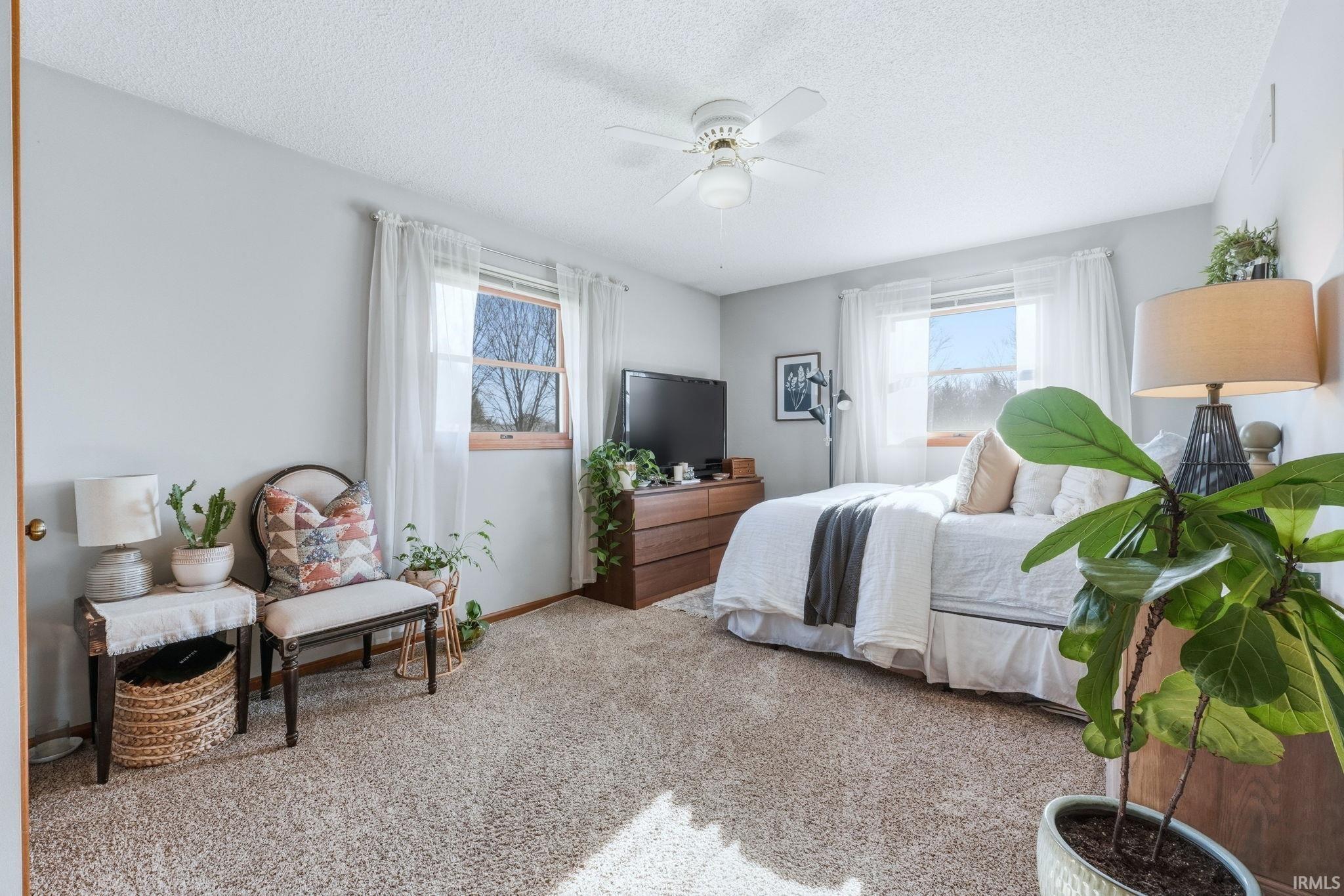 Bedroom with light carpet, multiple windows, ceiling fan, and a textured ceiling