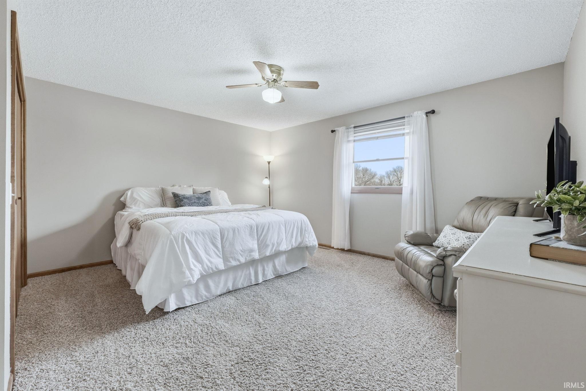 Bedroom with a textured ceiling, light carpet, and a ceiling fan