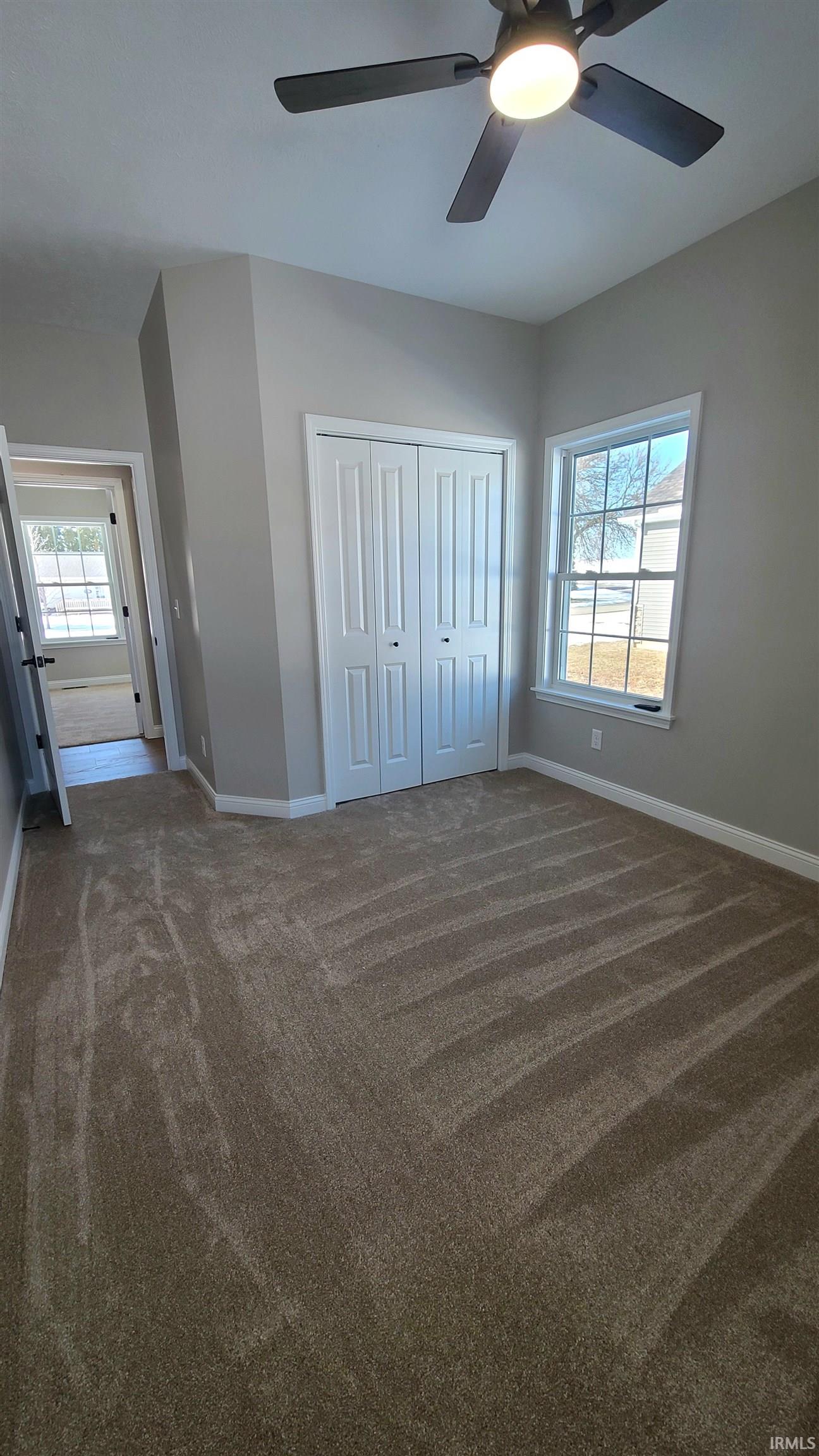 Unfurnished bedroom with dark colored carpet, a closet, multiple windows, and ceiling fan