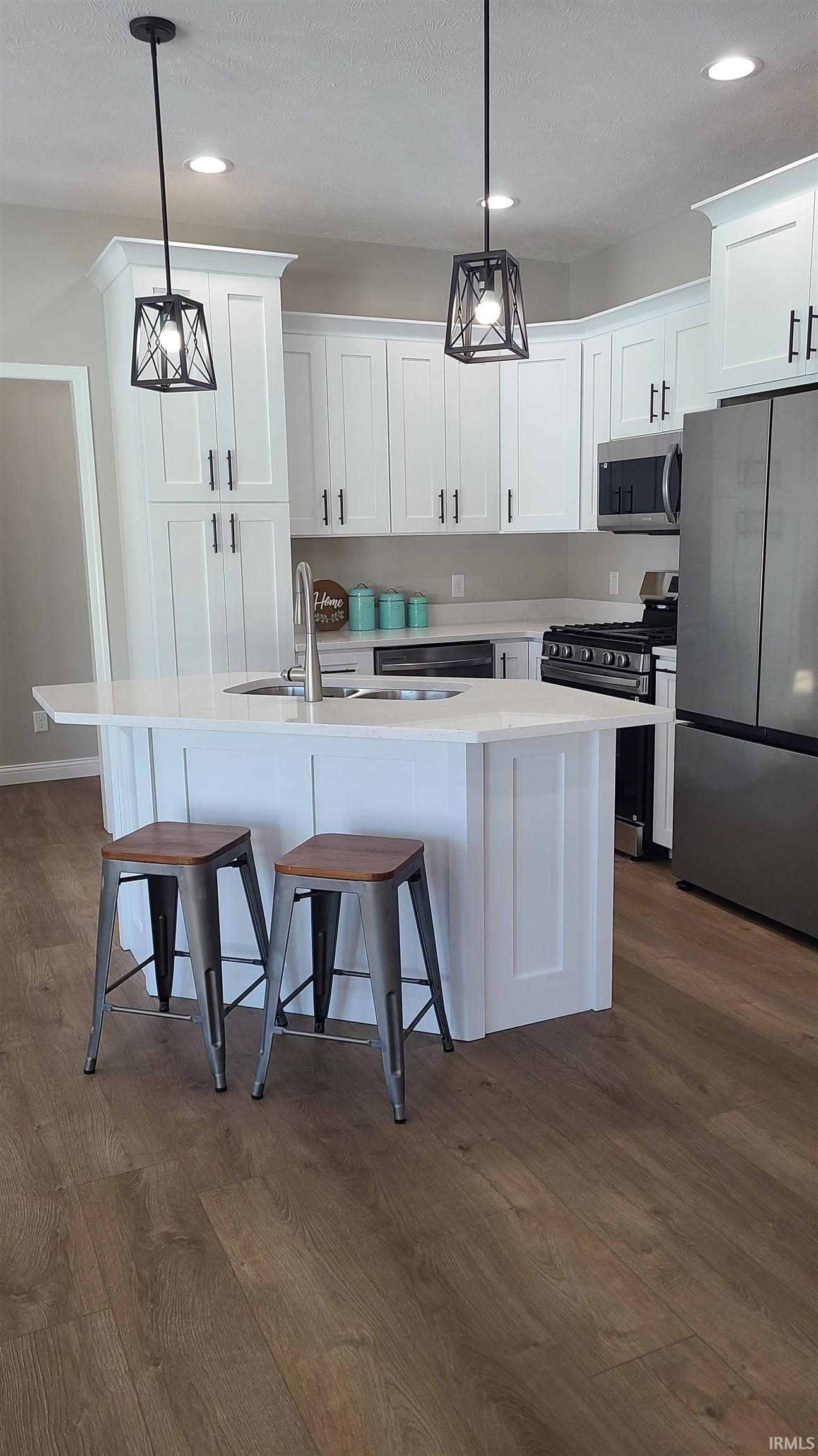 Kitchen featuring stainless steel appliances, a kitchen bar, white cabinetry, and dark wood-type flooring