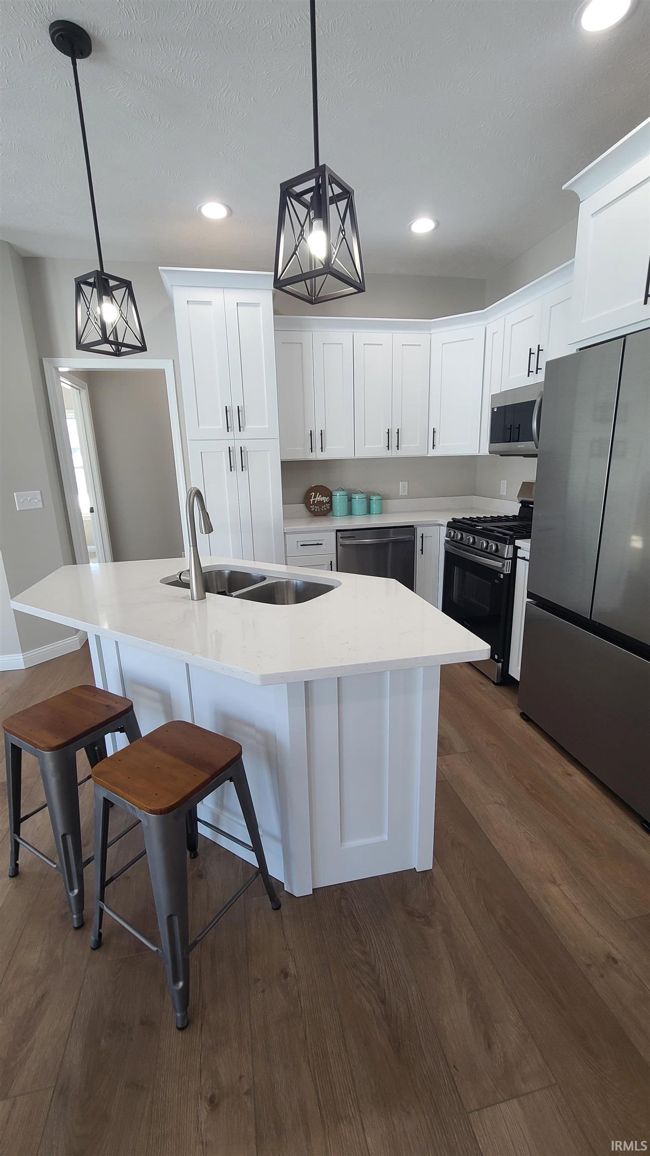 Kitchen with stainless steel appliances, white cabinetry, a kitchen breakfast bar, pendant lighting, and a center island with sink