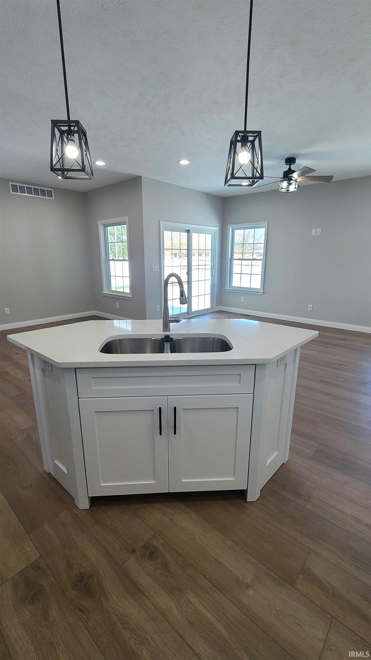 Kitchen with open floor plan, white cabinetry, dark wood-type flooring, a kitchen island with sink, and a textured ceiling