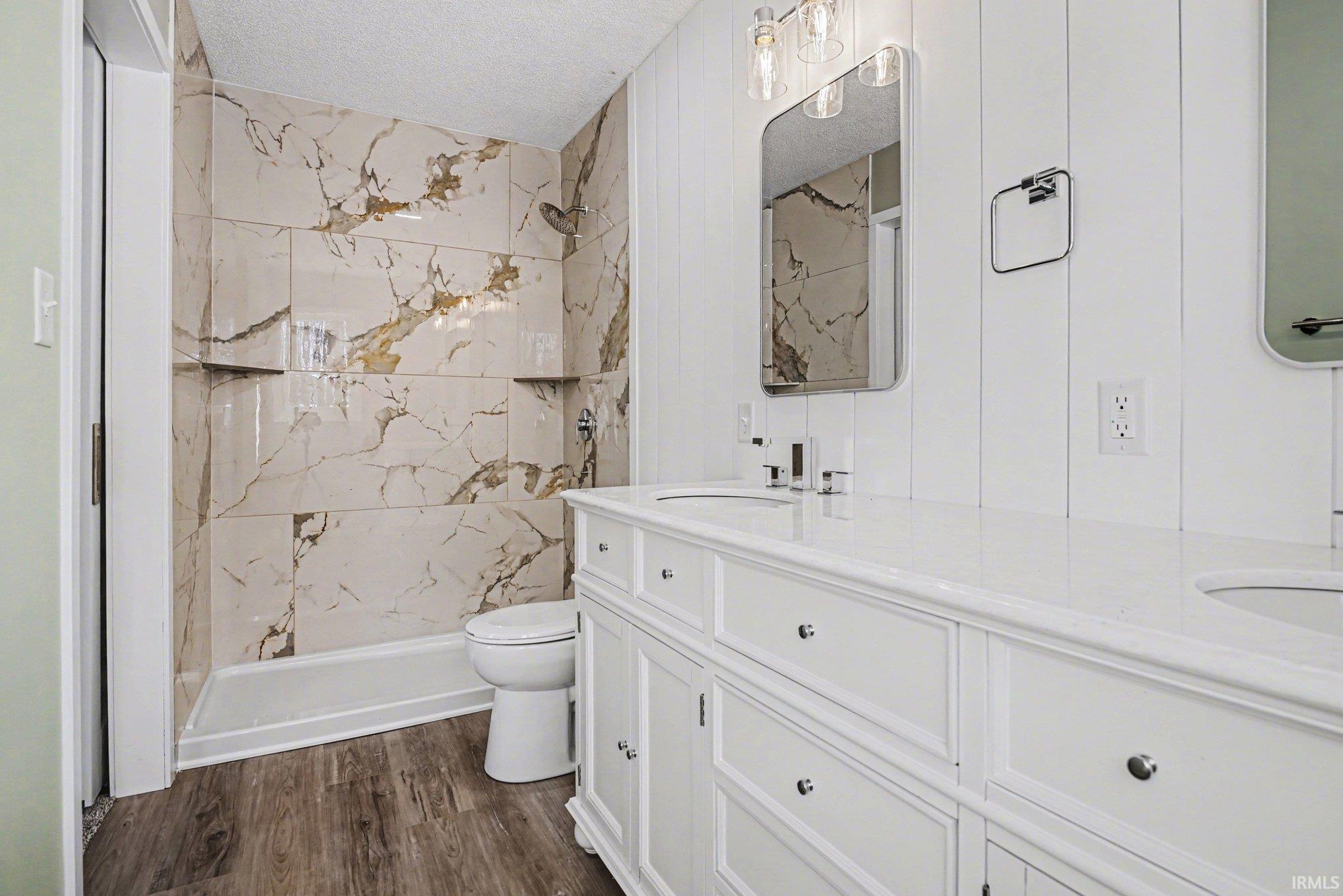 Bathroom featuring a marble finish shower, double vanity, a textured ceiling, and dark wood-style floors