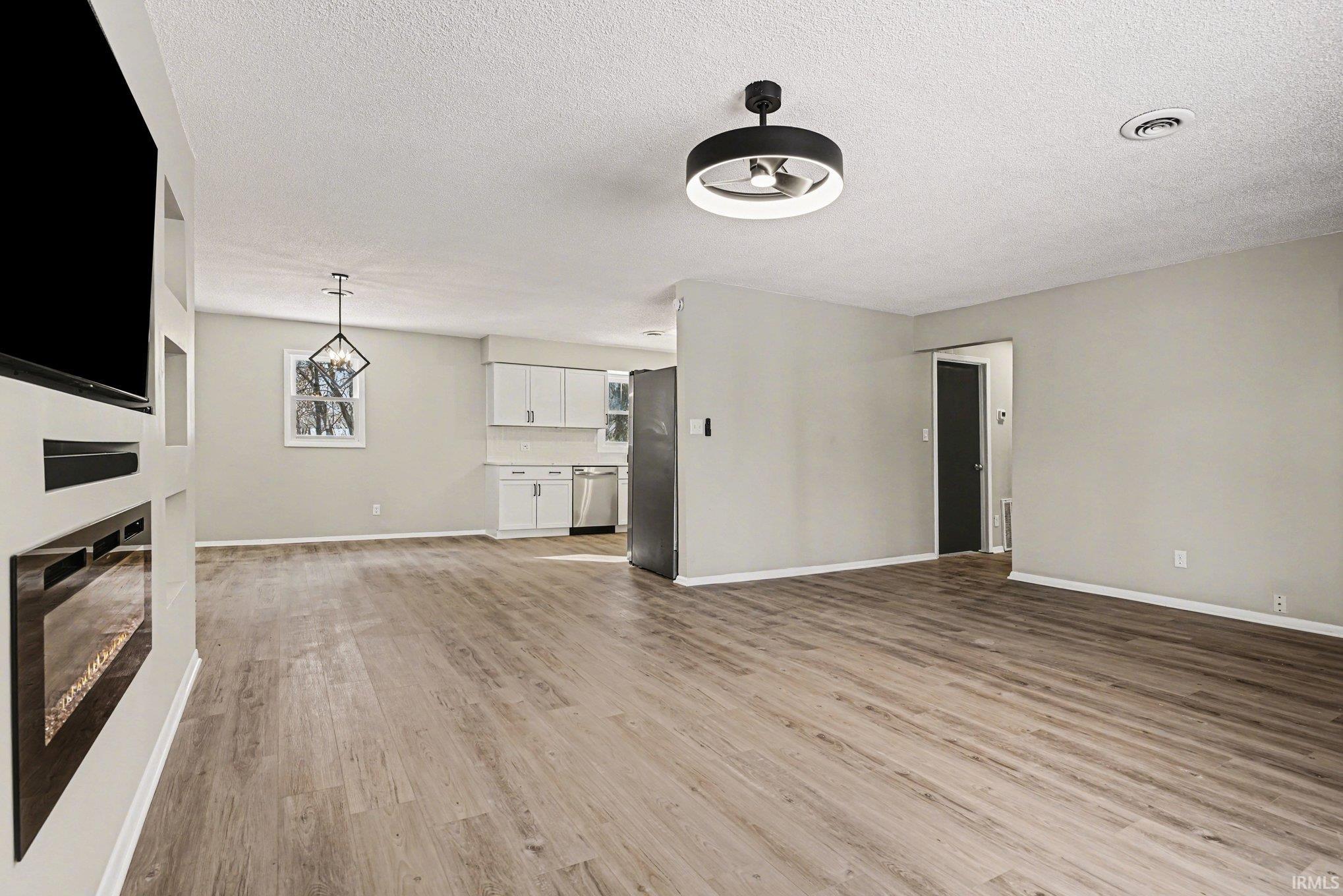 Unfurnished living room featuring a glass covered fireplace, light wood finished floors, and a textured ceiling