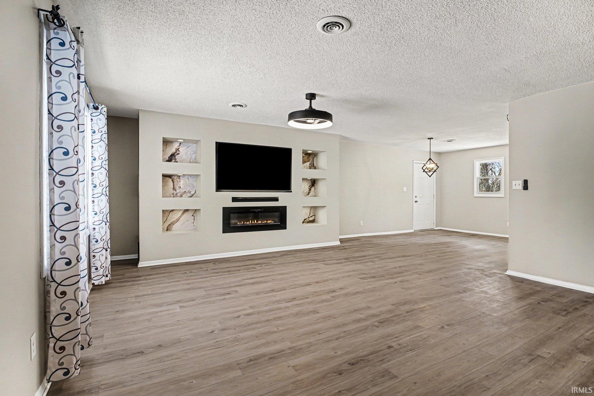 Unfurnished living room with built in features, wood finished floors, a glass covered fireplace, and a textured ceiling