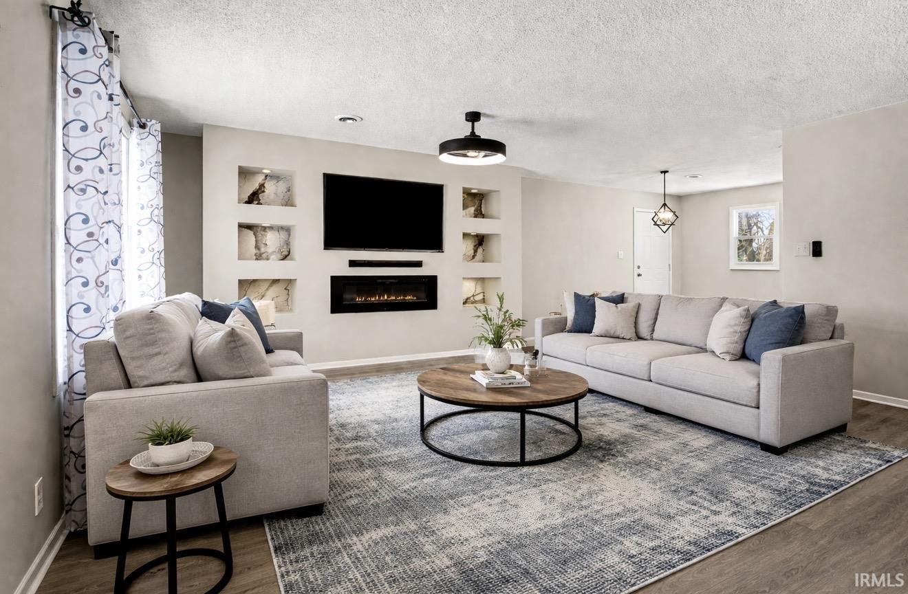 Living room featuring built in features, a textured ceiling, wood finished floors, and a glass covered fireplace