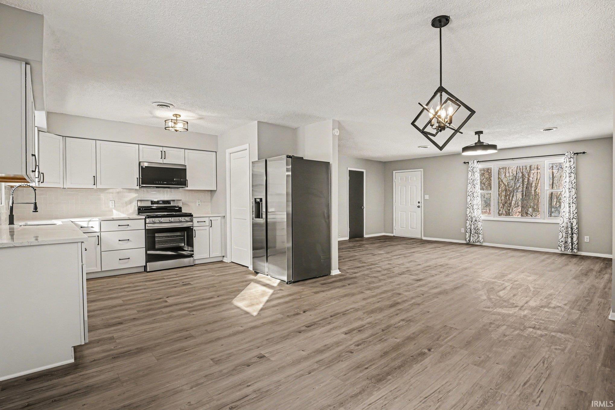 Kitchen featuring stainless steel appliances, white cabinetry, open floor plan, dark wood-style flooring, and tasteful backsplash