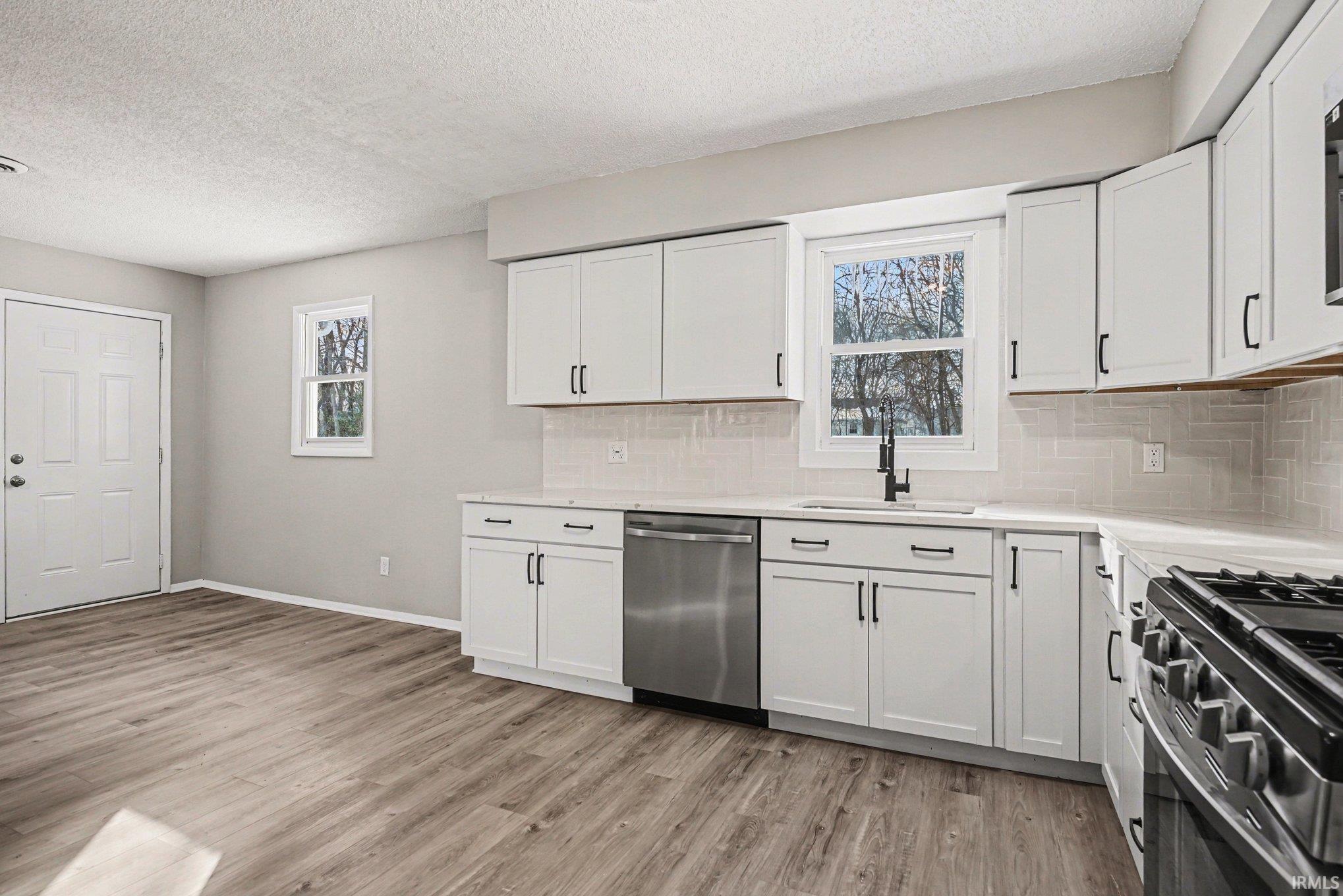 Kitchen with tasteful backsplash, stainless steel appliances, white cabinets, and a textured ceiling