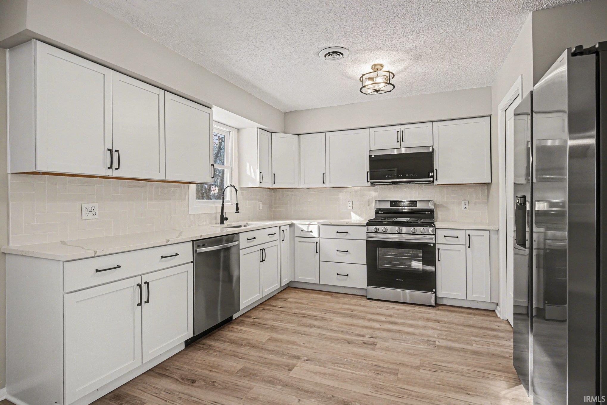 Kitchen with stainless steel appliances, white cabinets, light wood-style floors, backsplash, and light stone counters