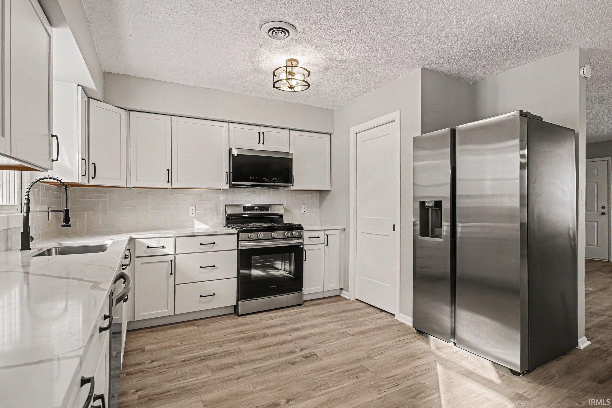 Kitchen with stainless steel appliances, light wood-type flooring, white cabinetry, light stone countertops, and a textured ceiling