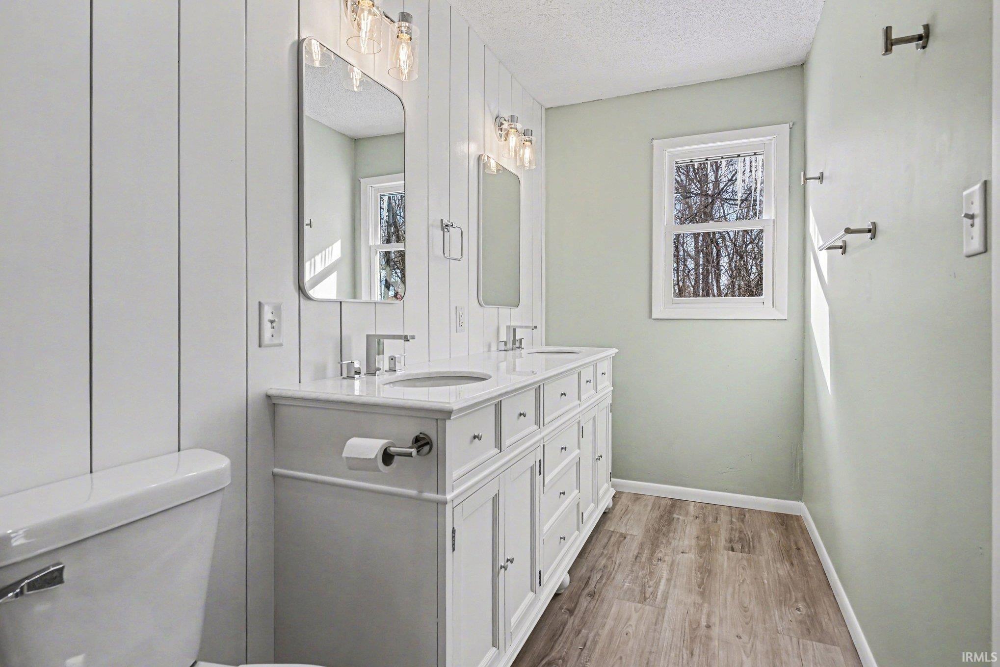 Full bathroom featuring double vanity, light wood-style floors, and a textured ceiling