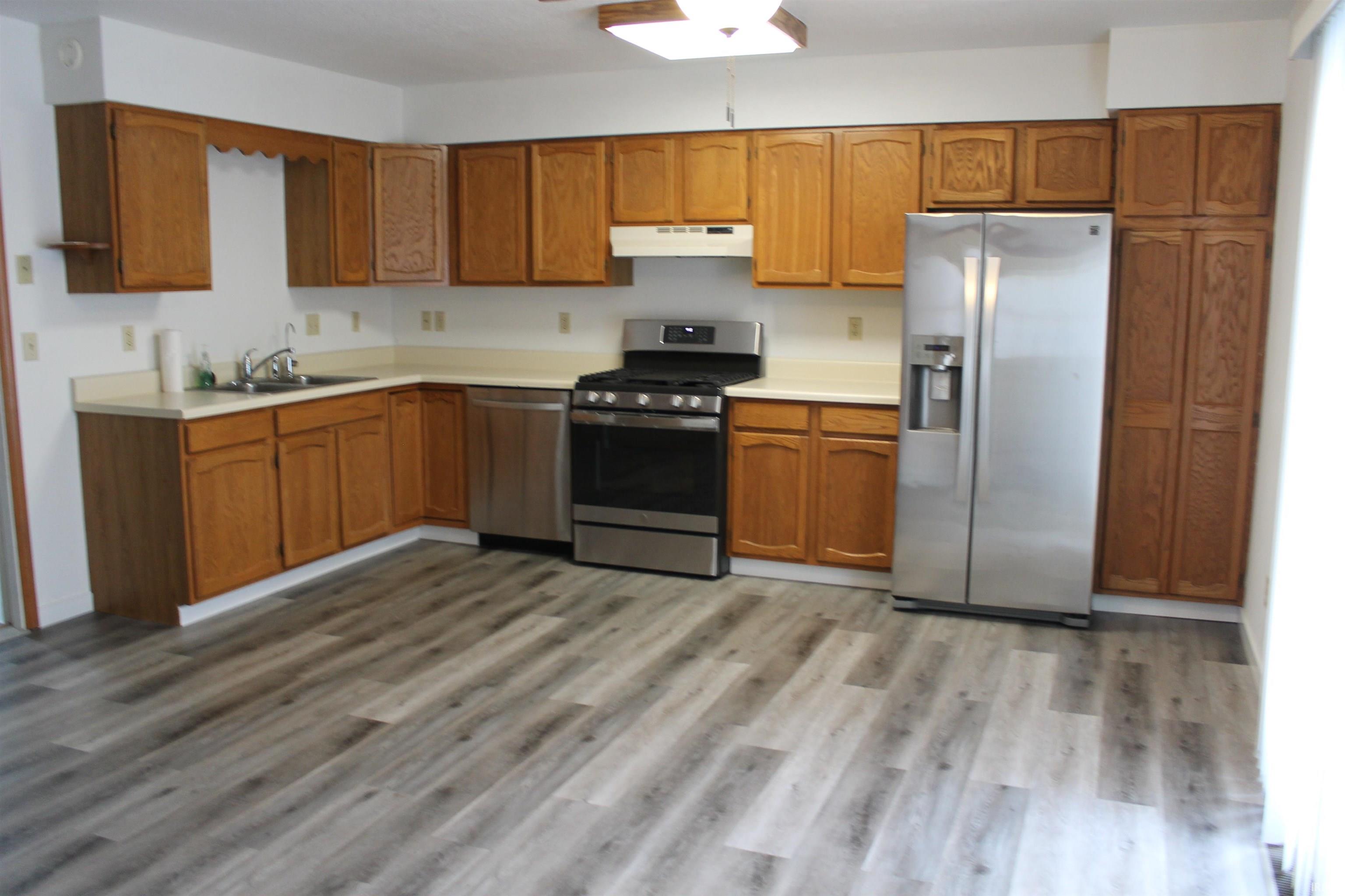 Kitchen with stainless steel appliances, light countertops, wood finish cabinetry, dark wood finished floors, and a ceiling fan