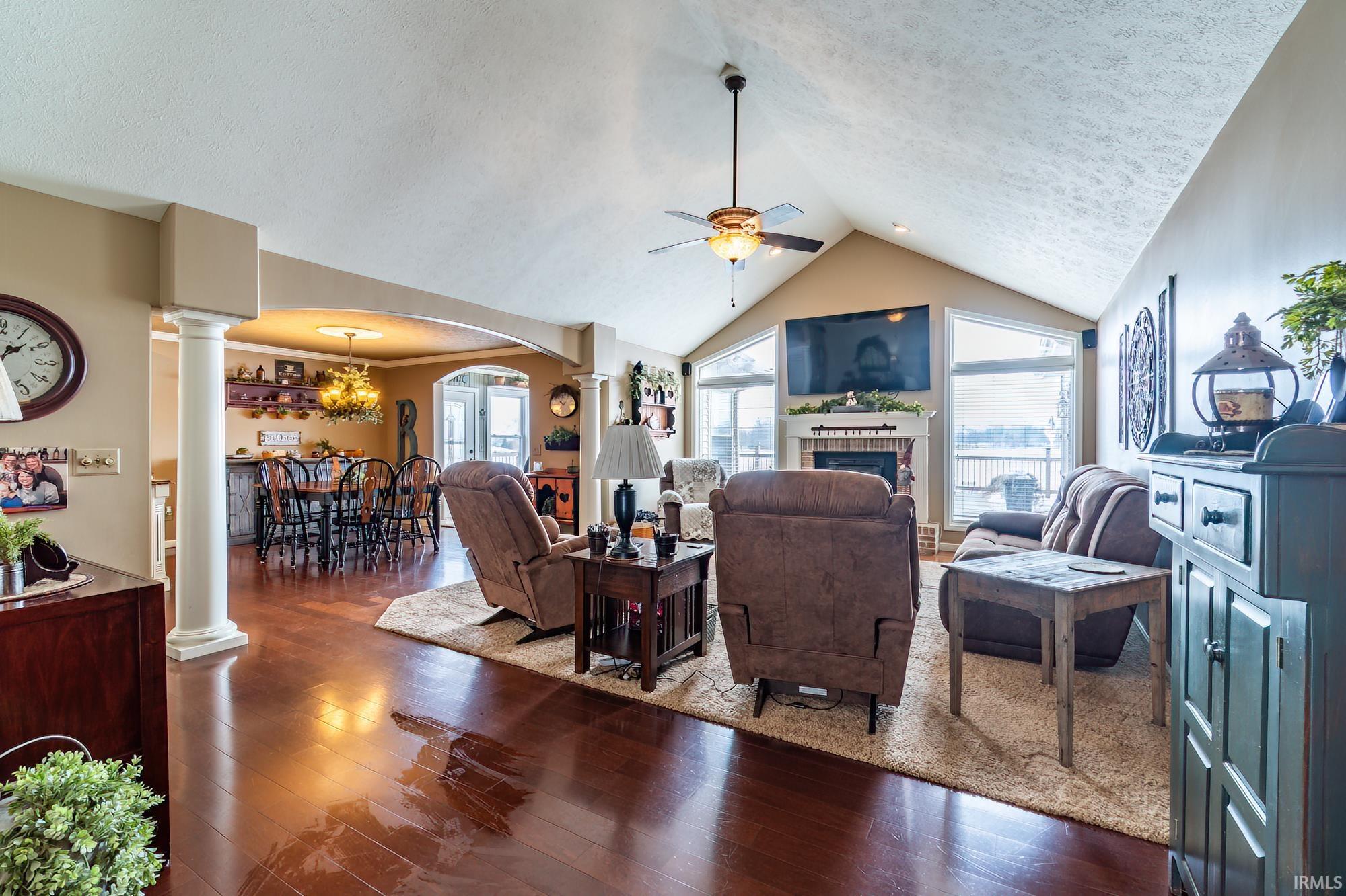 Living area with ornate columns, dark wood-style flooring, a textured ceiling, arched walkways, and a ceiling fan