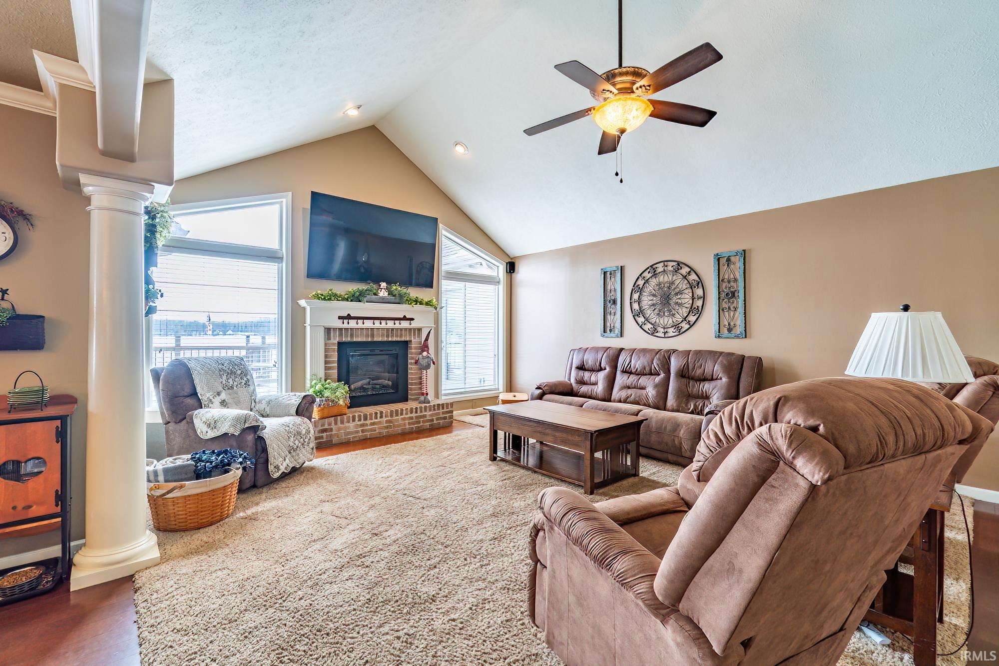 Living room featuring decorative columns, a ceiling fan, and a fireplace with lake views