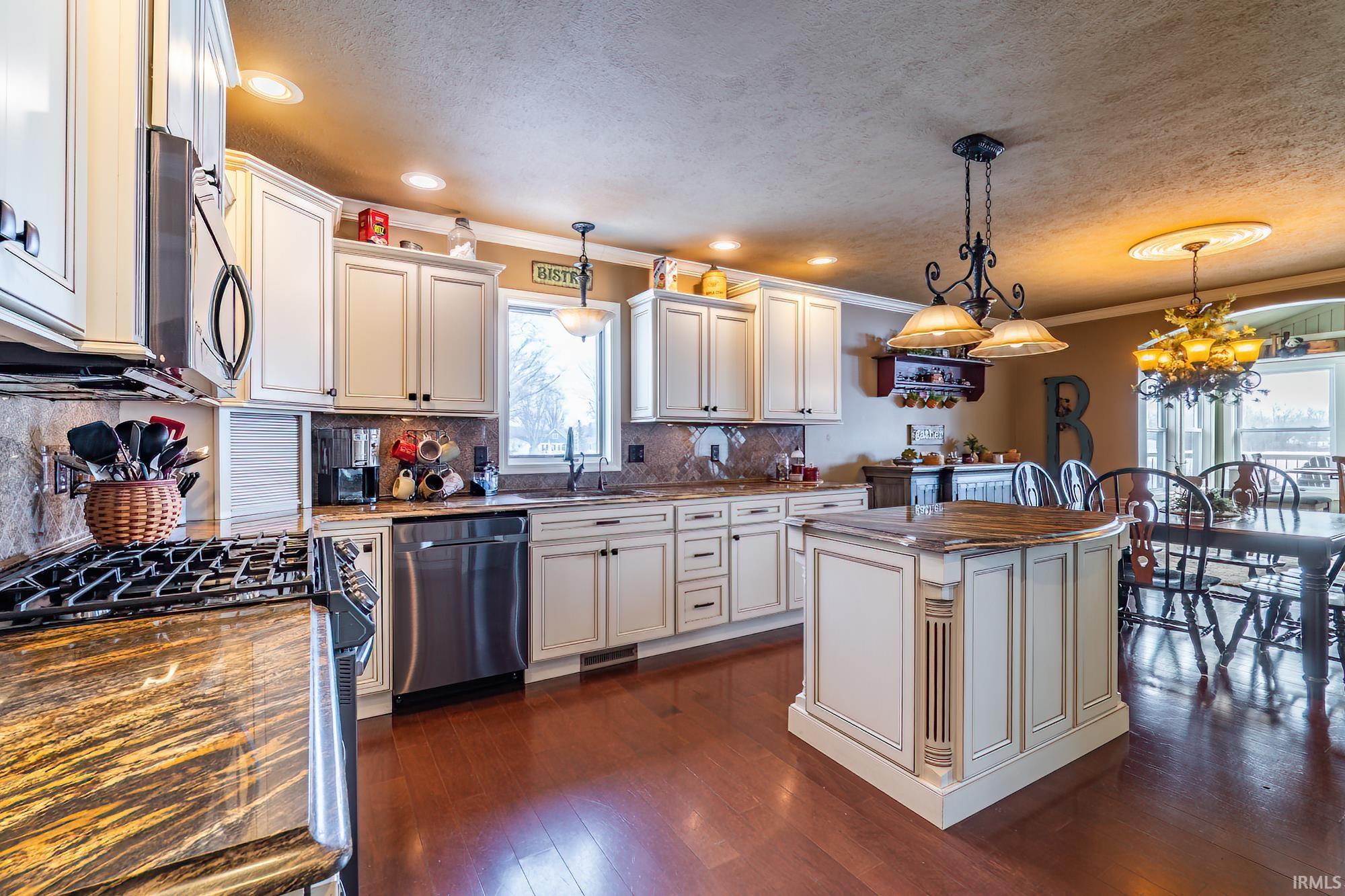 Kitchen featuring stainless steel appliances, a center island, dark stone countertops, crown molding, and dark wood-style floors