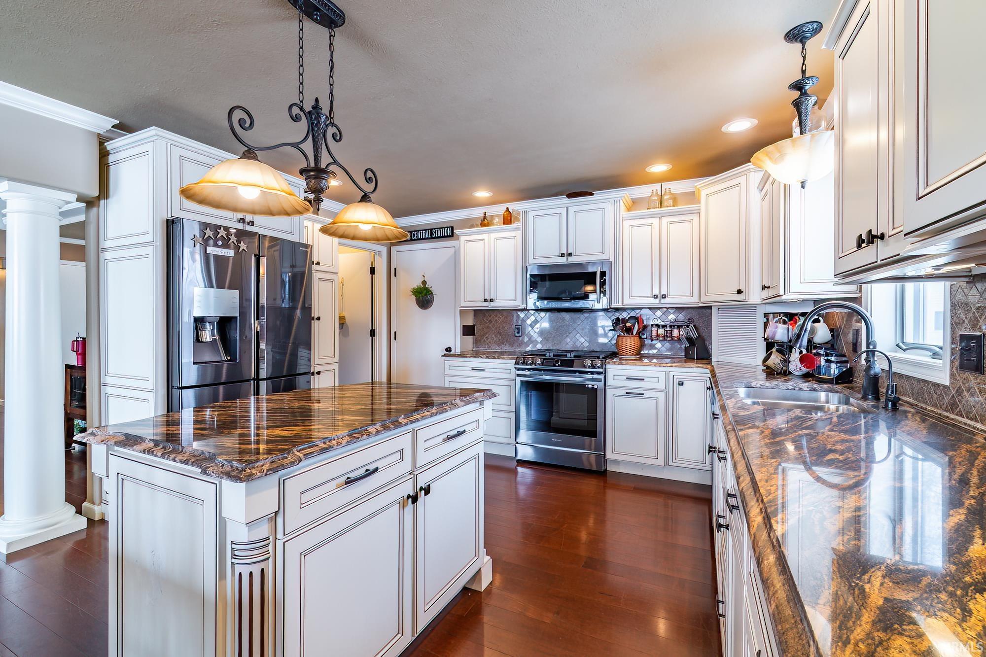 Kitchen featuring decorative light fixtures, stainless steel appliances, dark stone counters, ornamental molding, and a center island