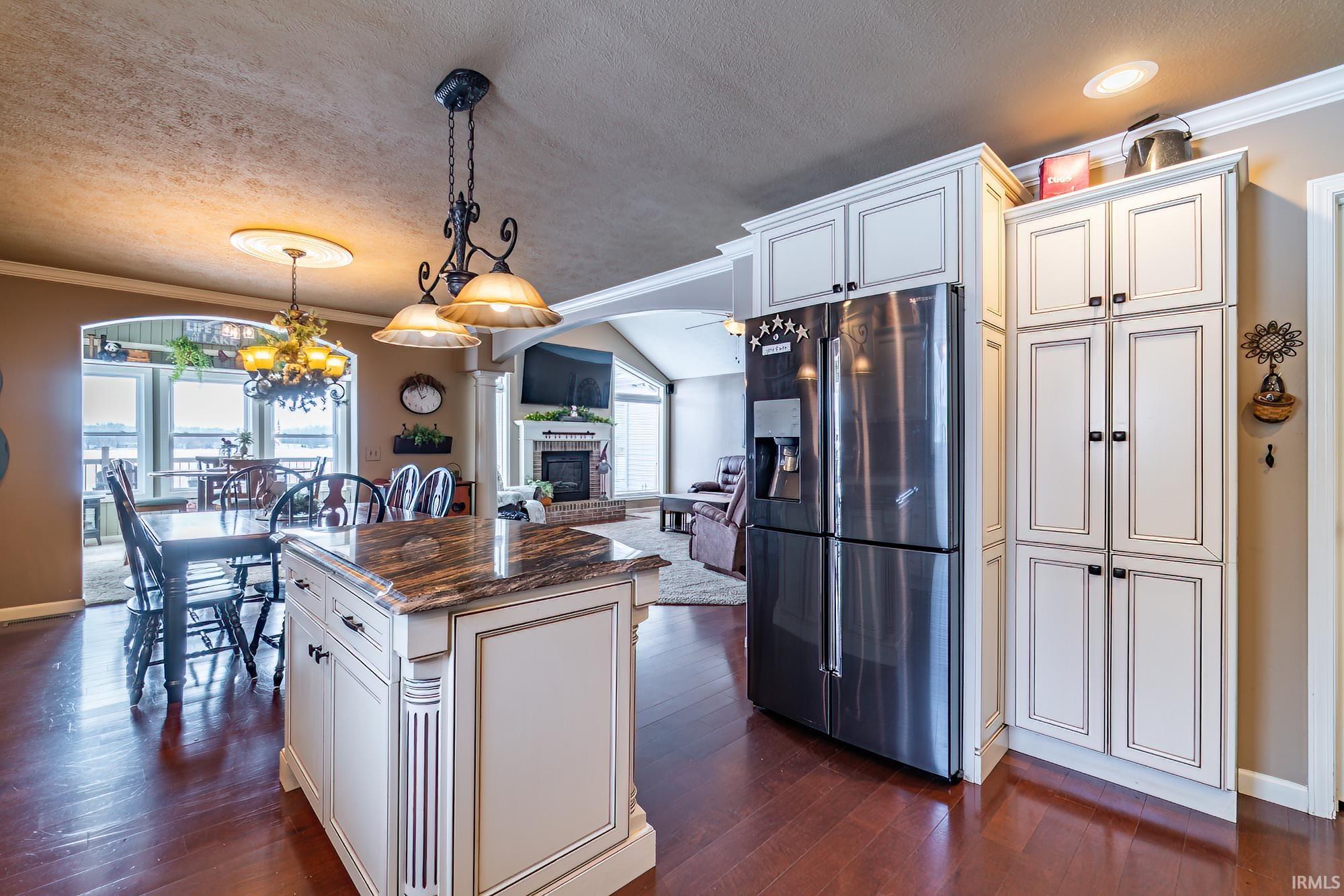 Kitchen with ornamental molding, stainless steel fridge, a textured ceiling, a kitchen island, and dark stone counters with an eat in kitchen area overlooking the lake views
