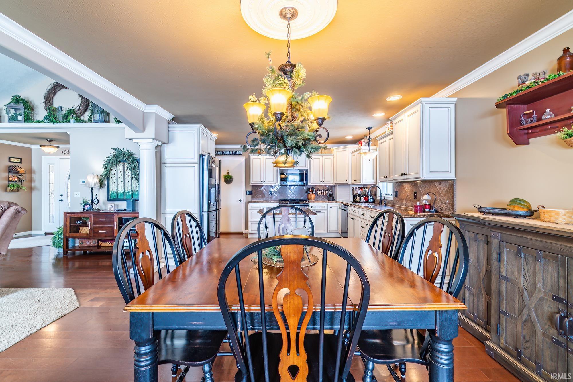 Dining area with ornamental molding, suspended lighting, dark wood finished floors, and ornate columns