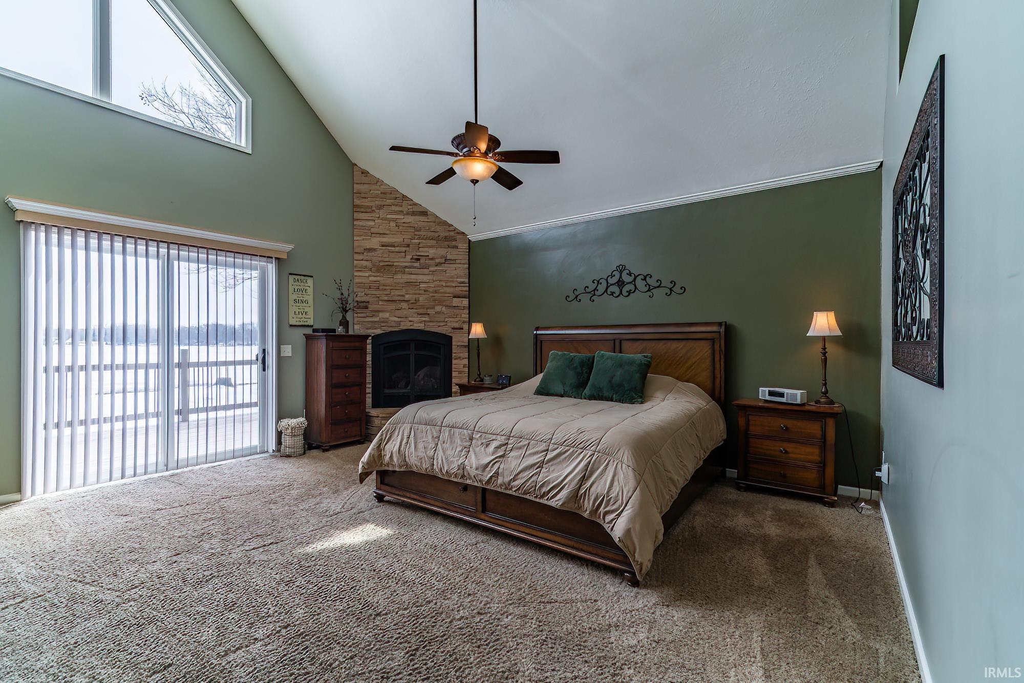 Bedroom with carpet flooring, vaulted ceiling, ceiling fan, a fireplace, and access to outside