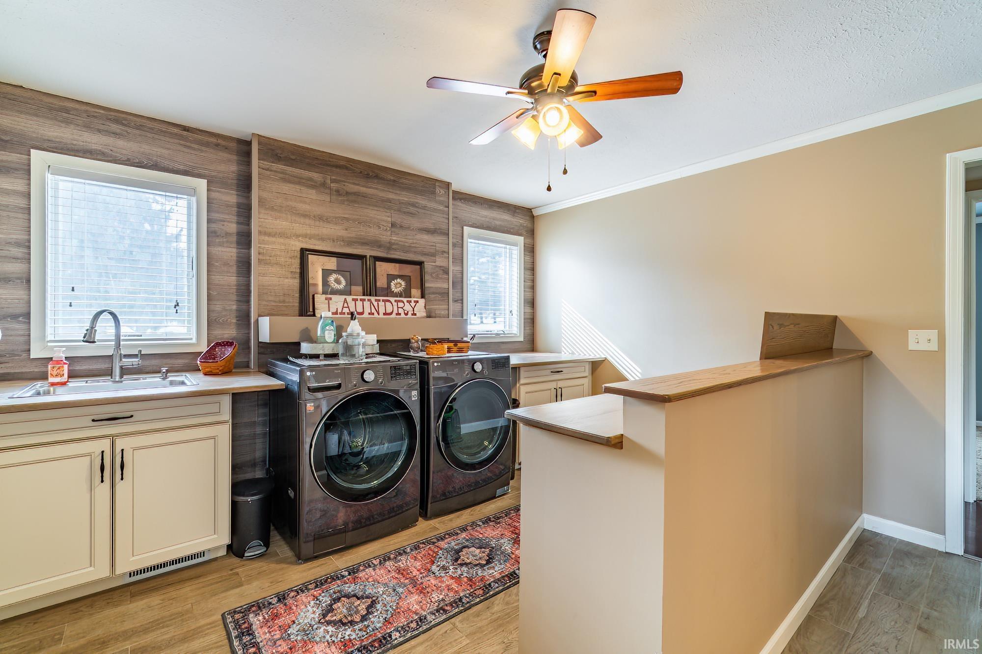 Laundry area with washer and dryer, light wood finished floors, ceiling fan, ornamental molding, and wood walls