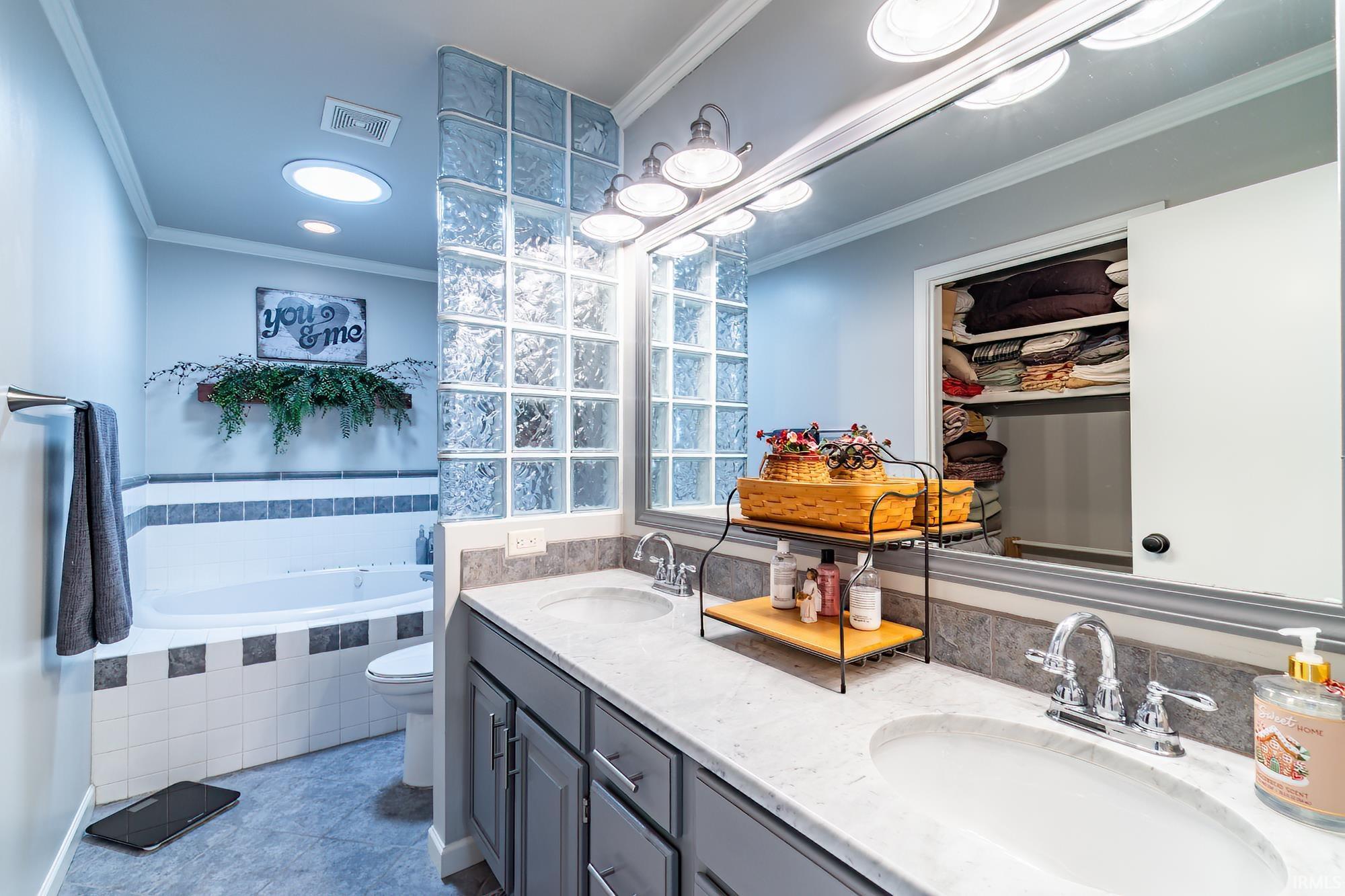 Bathroom with crown molding, double vanity, a bath, and tile patterned flooring