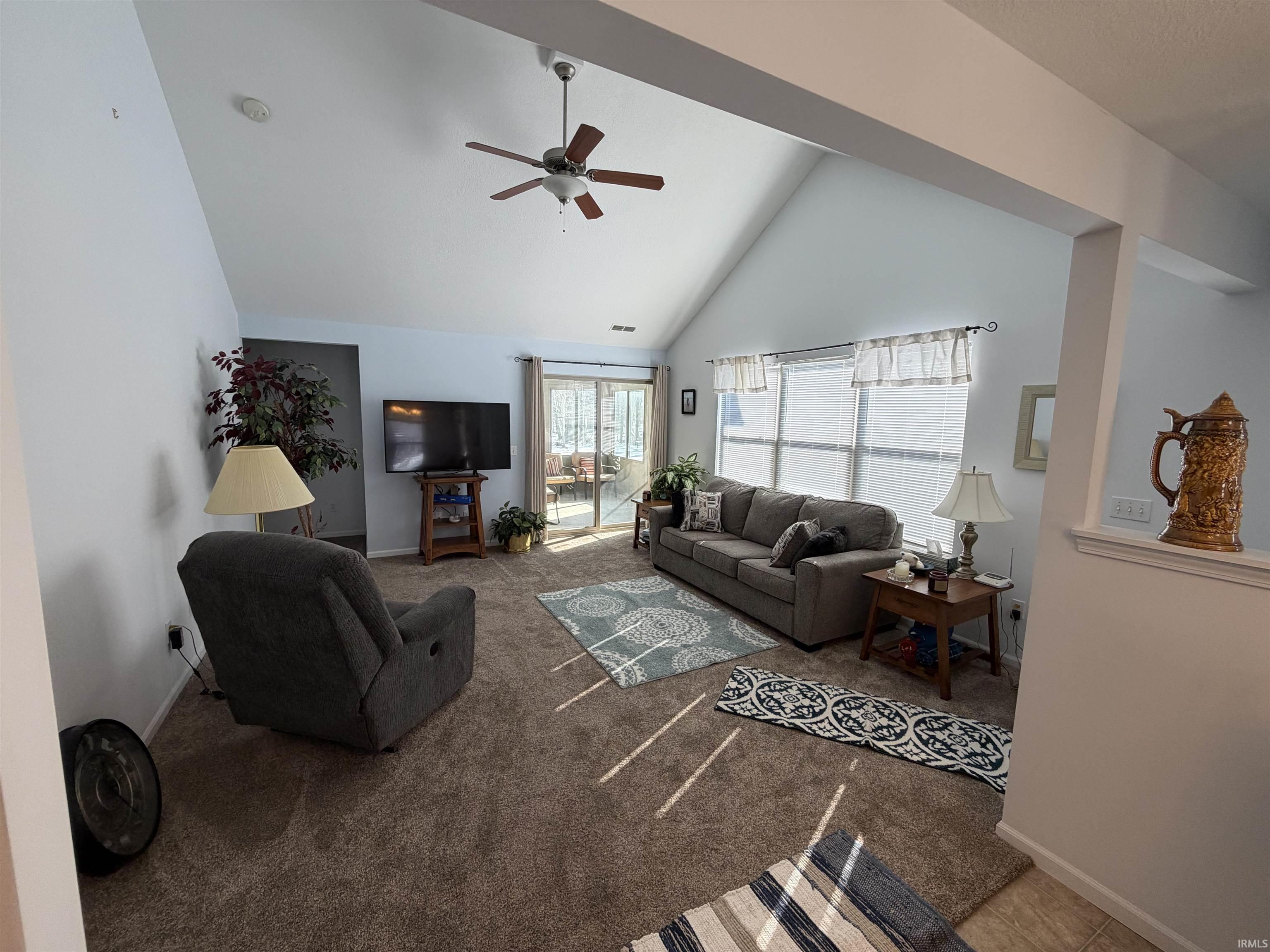 Living area featuring carpet floors, ceiling fan, and vaulted ceiling