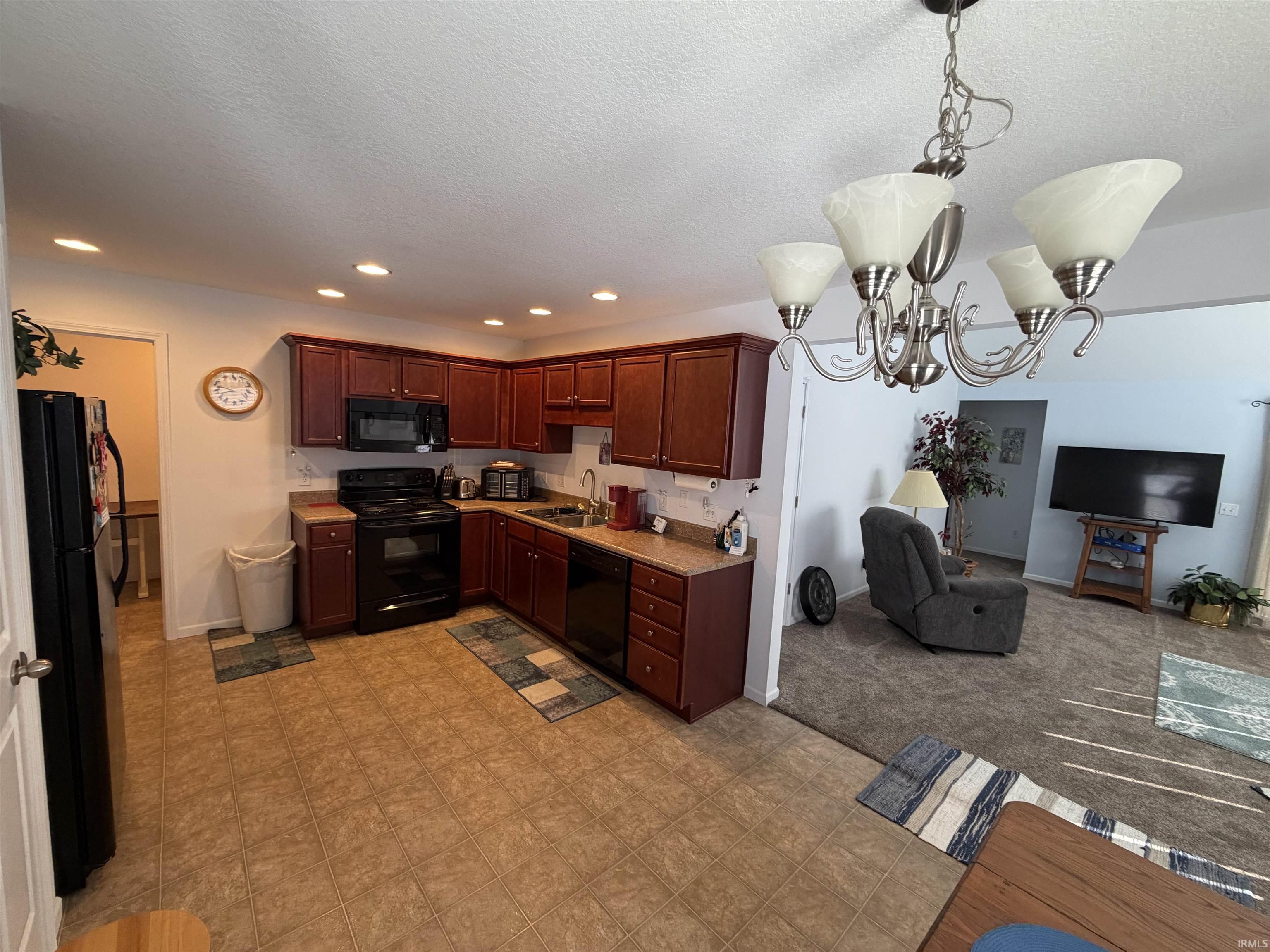 Kitchen with black appliances, hanging lights, light countertops, open floor plan, and a textured ceiling