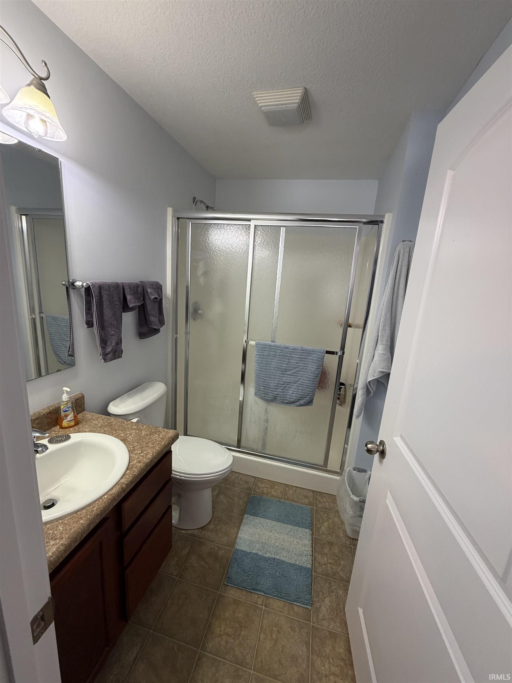 Bathroom with vanity, a stall shower, a textured ceiling, and dark tile patterned flooring