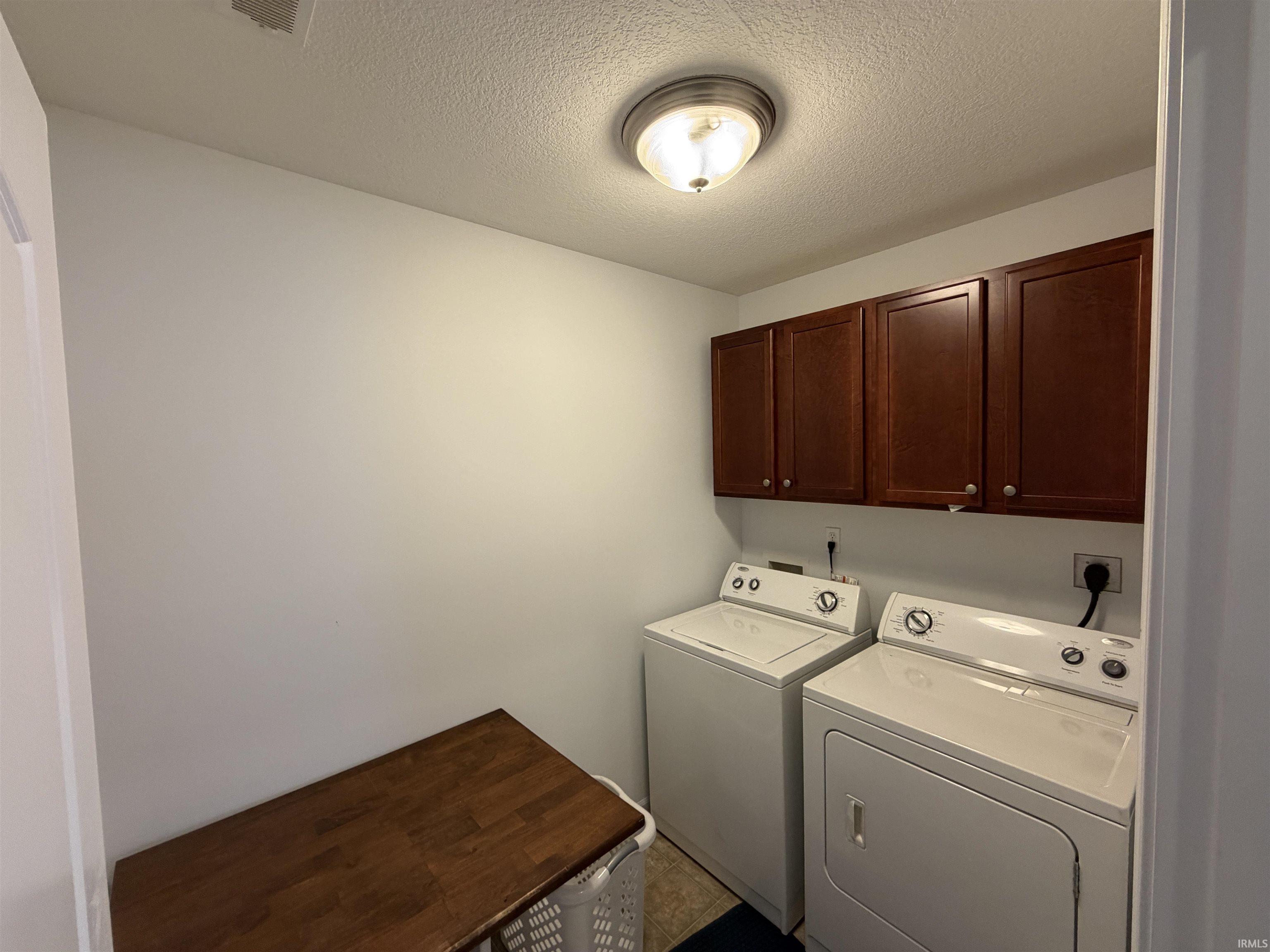 Laundry area featuring a textured ceiling, cabinet space, and washer and clothes dryer