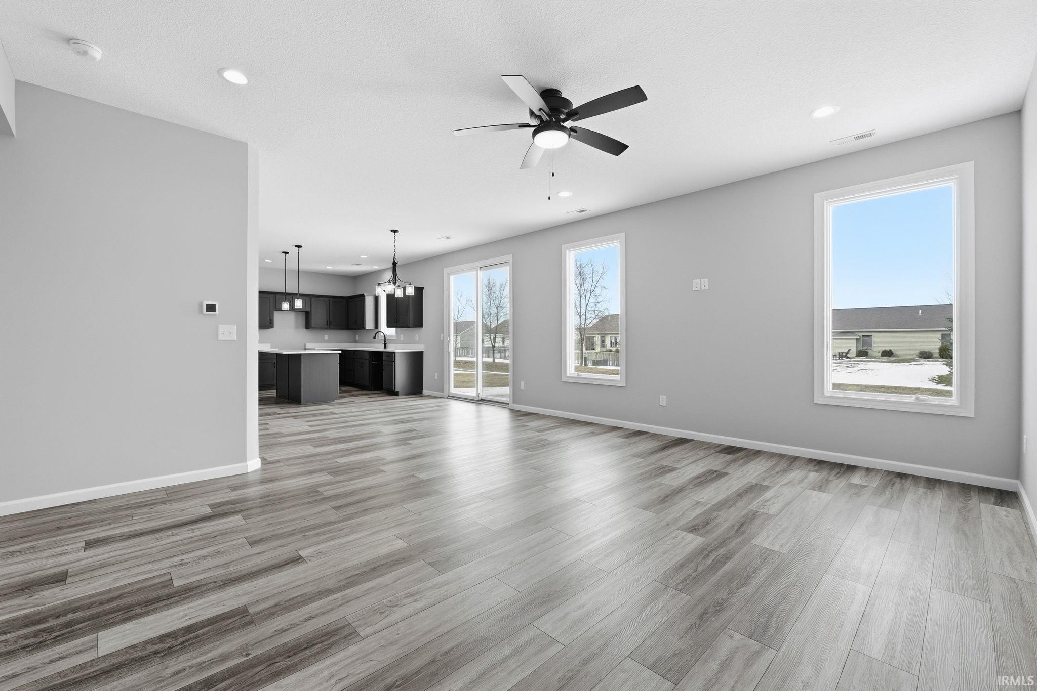 Unfurnished living room with ceiling fan, suspended lighting, and light wood-style flooring