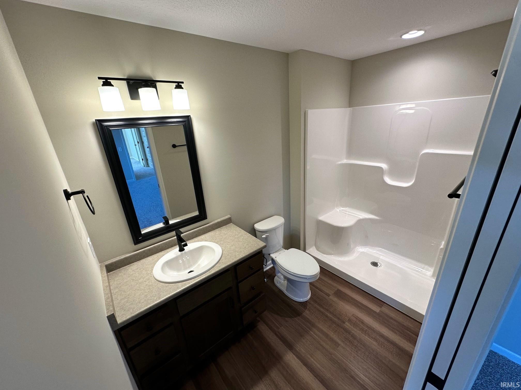 Full bath featuring vanity, a shower stall, dark wood-style floors, and a textured ceiling