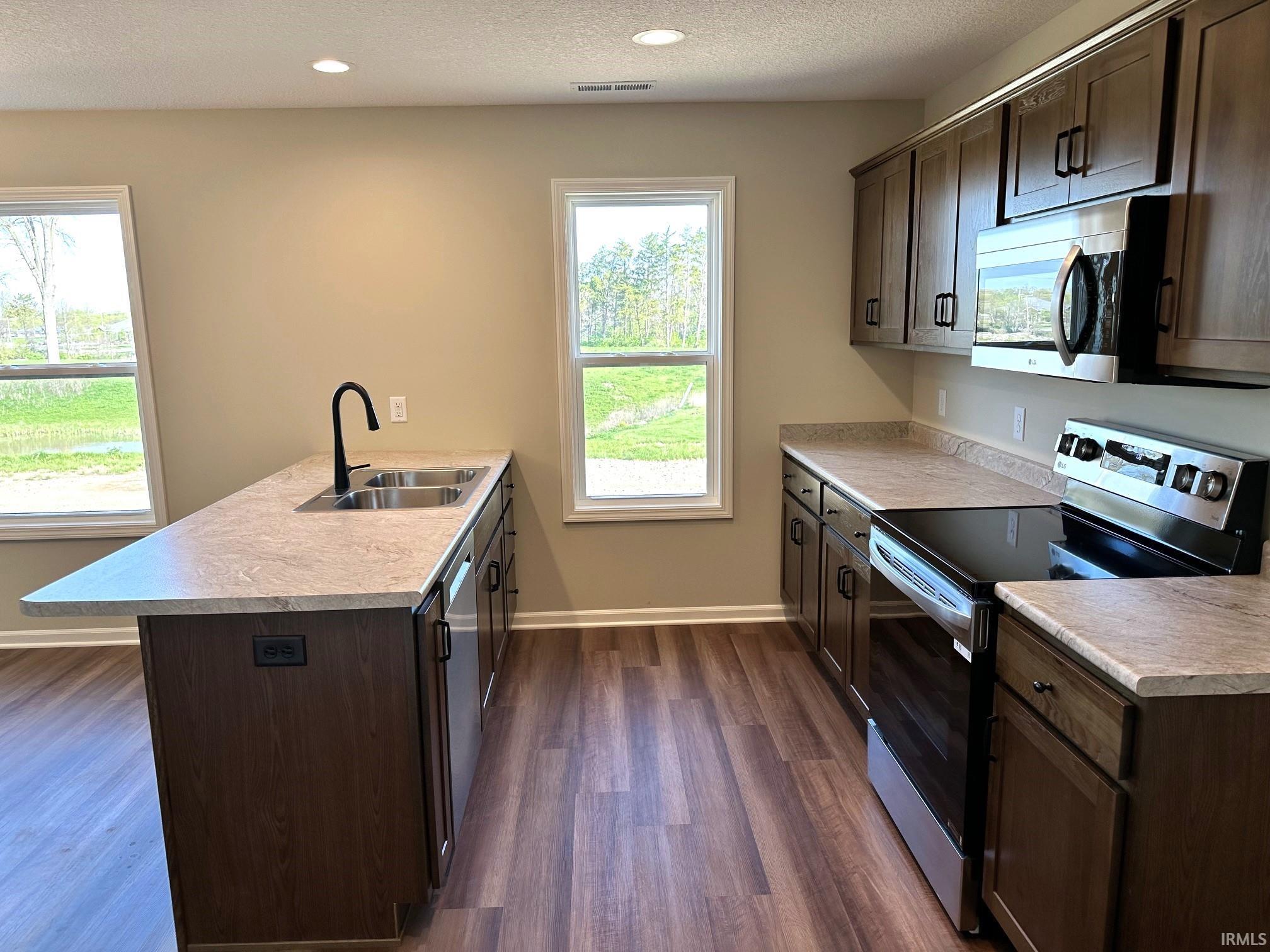 Kitchen with stainless steel appliances, dark wood finish cabinets, a peninsula, light countertops, and a textured ceiling